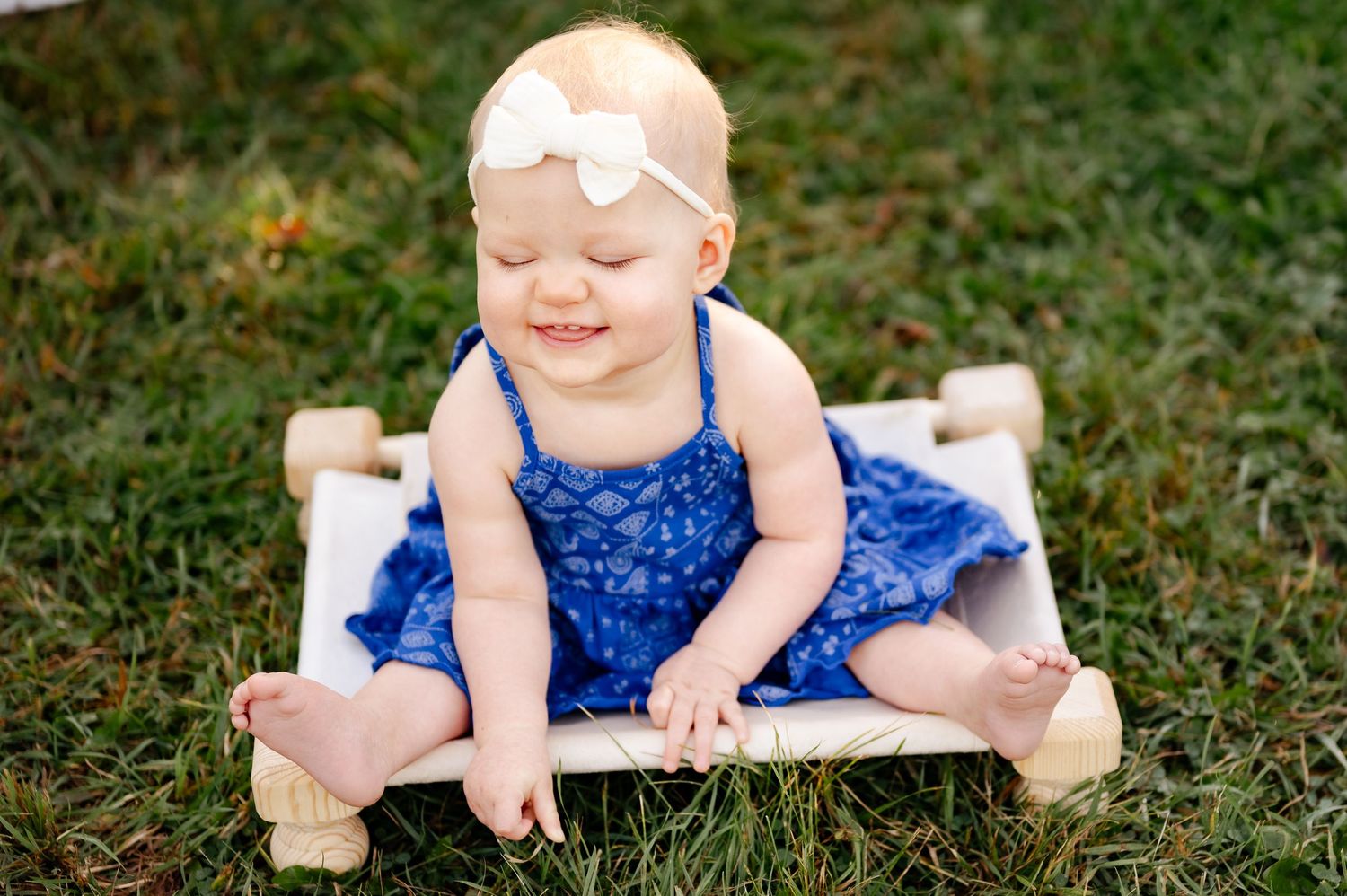A small child in a navy dress sits on a white platform outdoors.