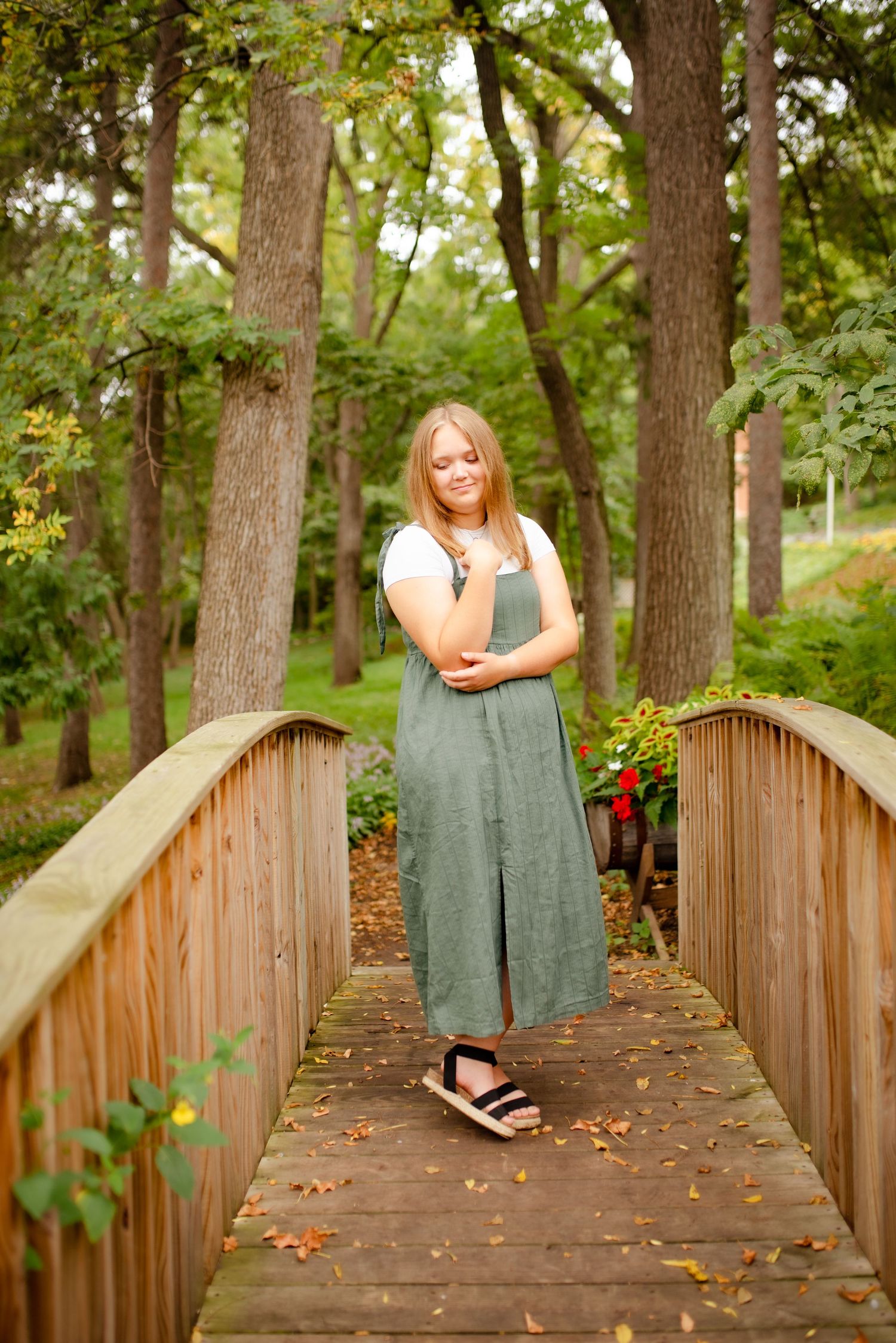 Person in gray dress standing on wooden bridge surrounded by lush forest.