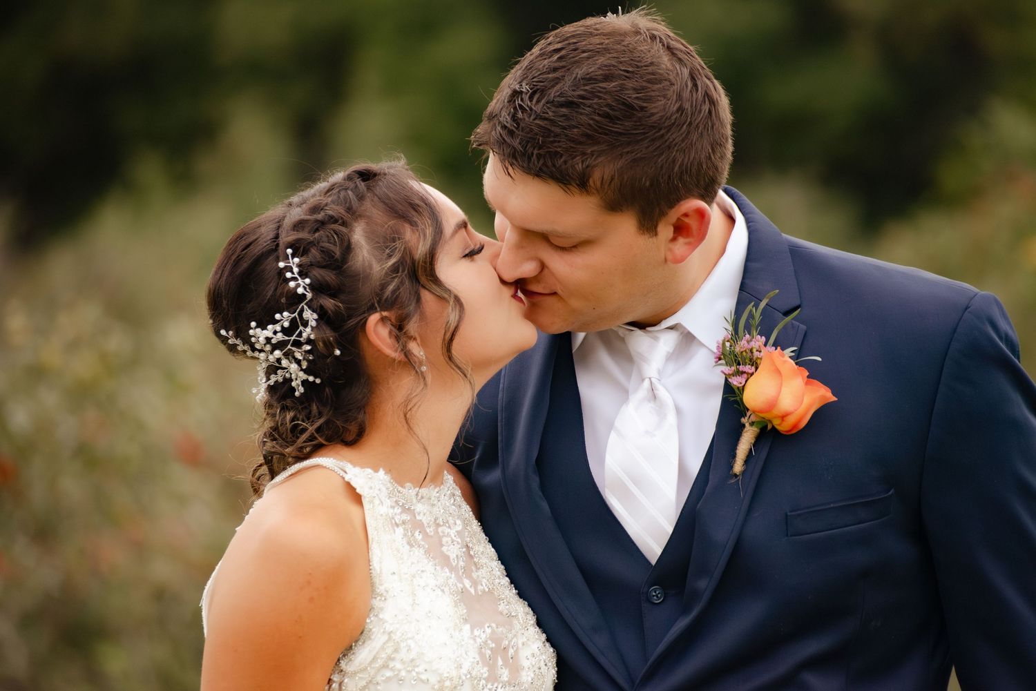 Bride and groom share an intimate kiss outdoors with delicate floral details in her hair.