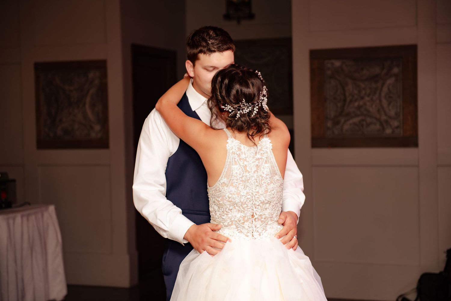 Intimate dance moment showing detailed lace back of wedding gown in dimly lit reception space.