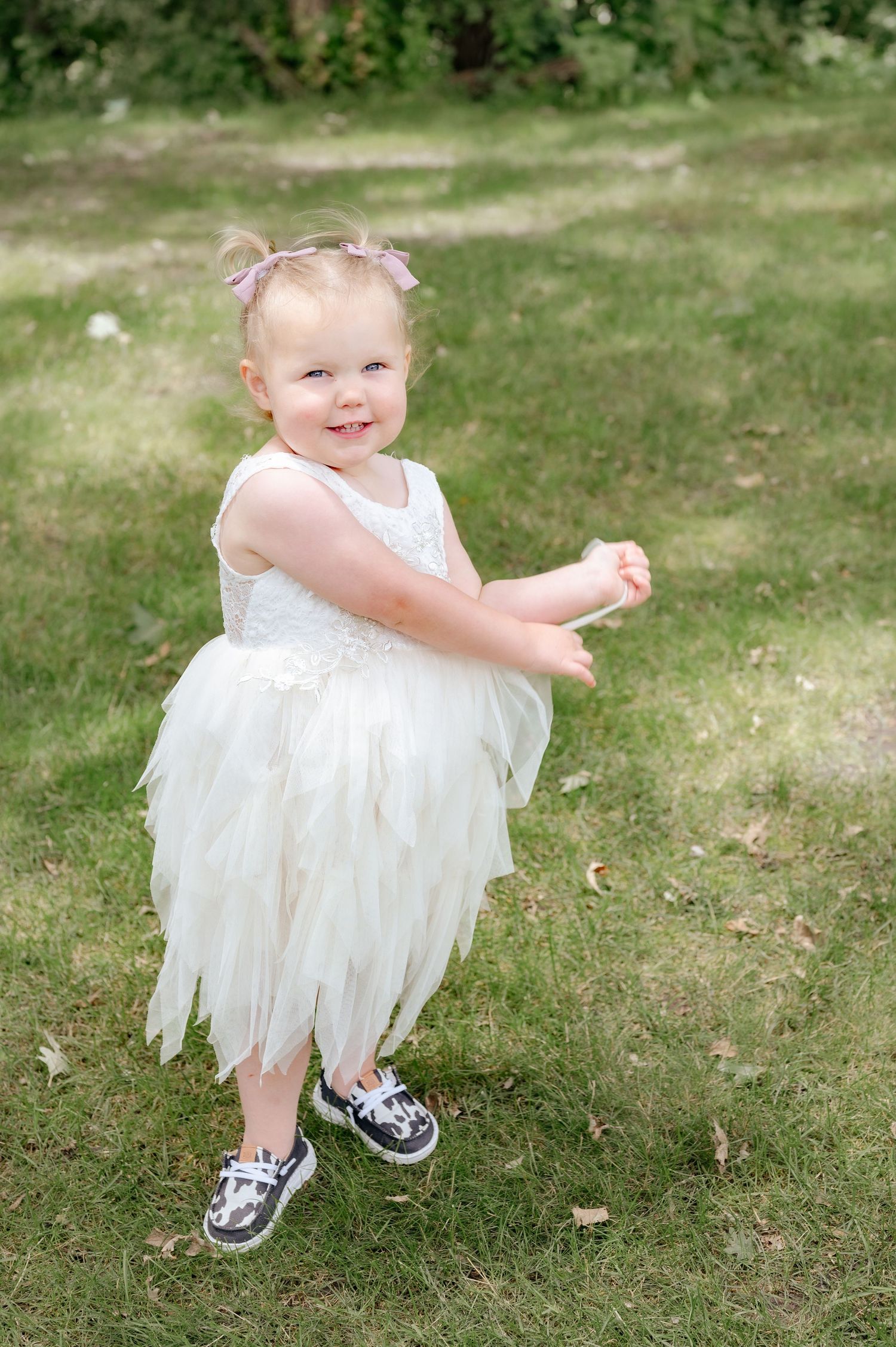Young child in white tulle dress and sneakers twirling outdoors.