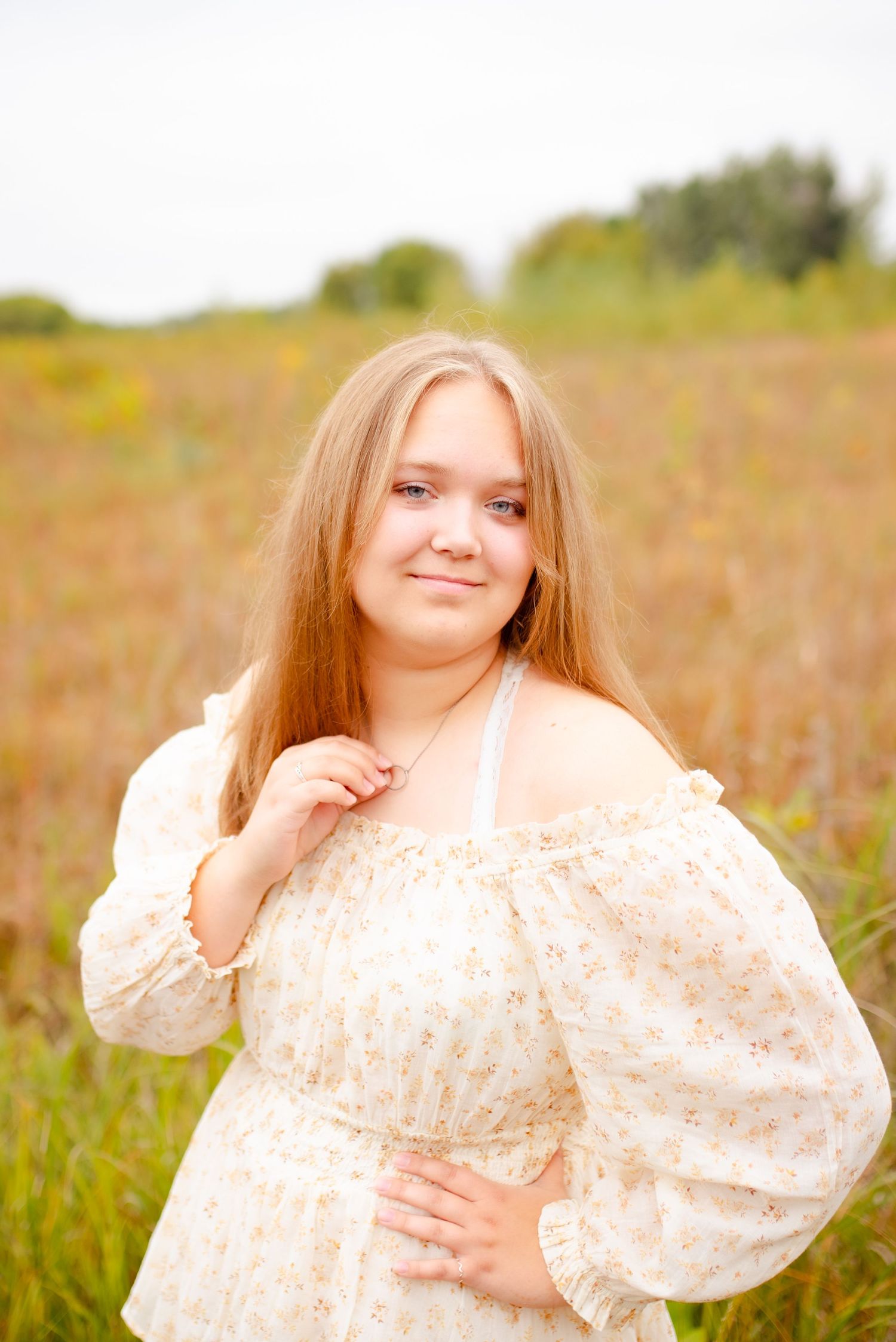 Portrait in a floral cream dress standing in a sunlit field of tall grass.