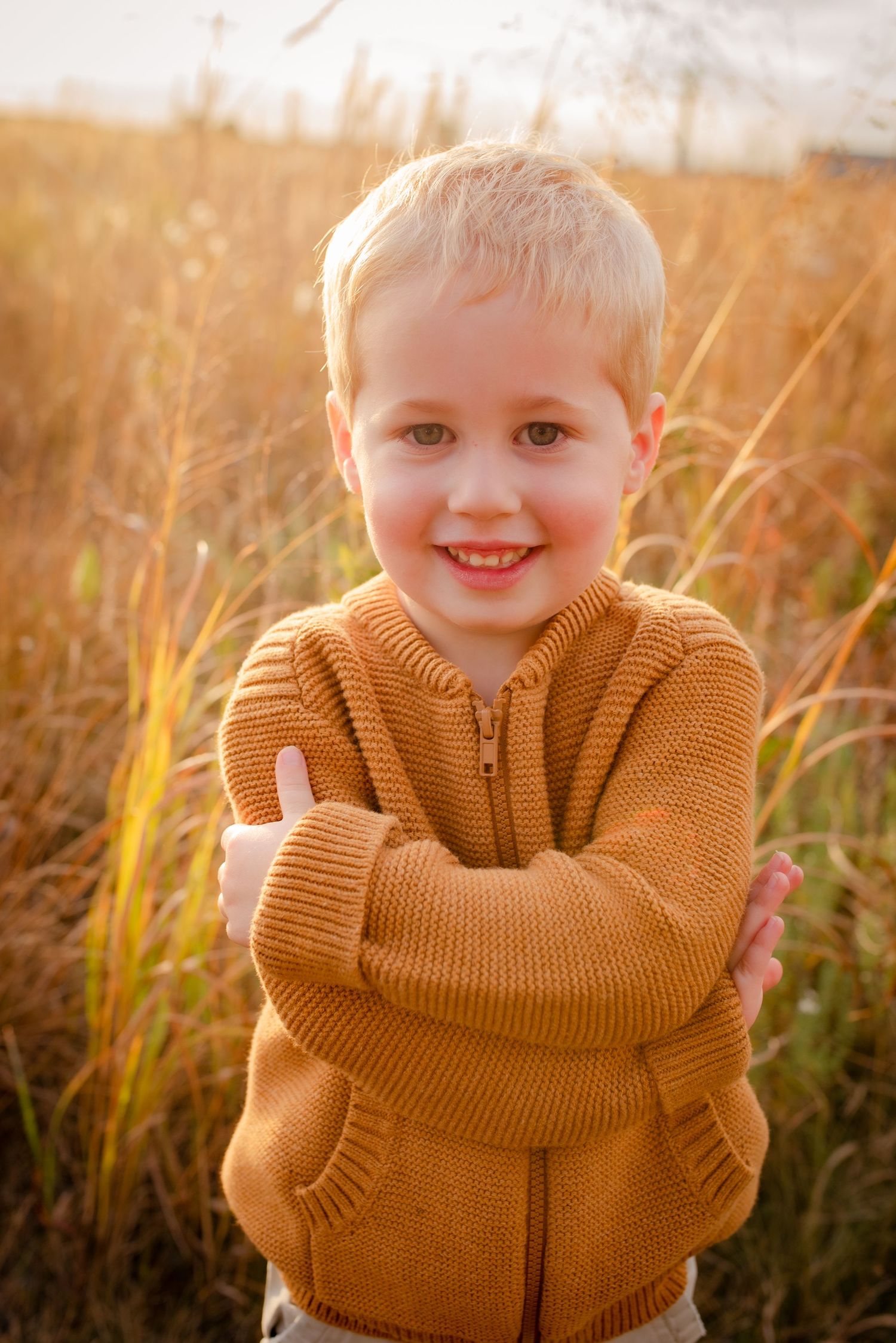 Young child in orange sweater smiles warmly in golden backlit field.
