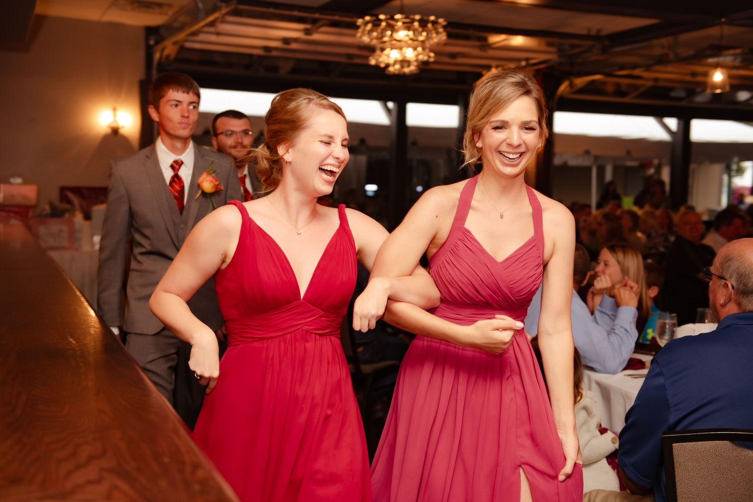 Bridesmaids in red dresses dancing and laughing at a wedding reception.