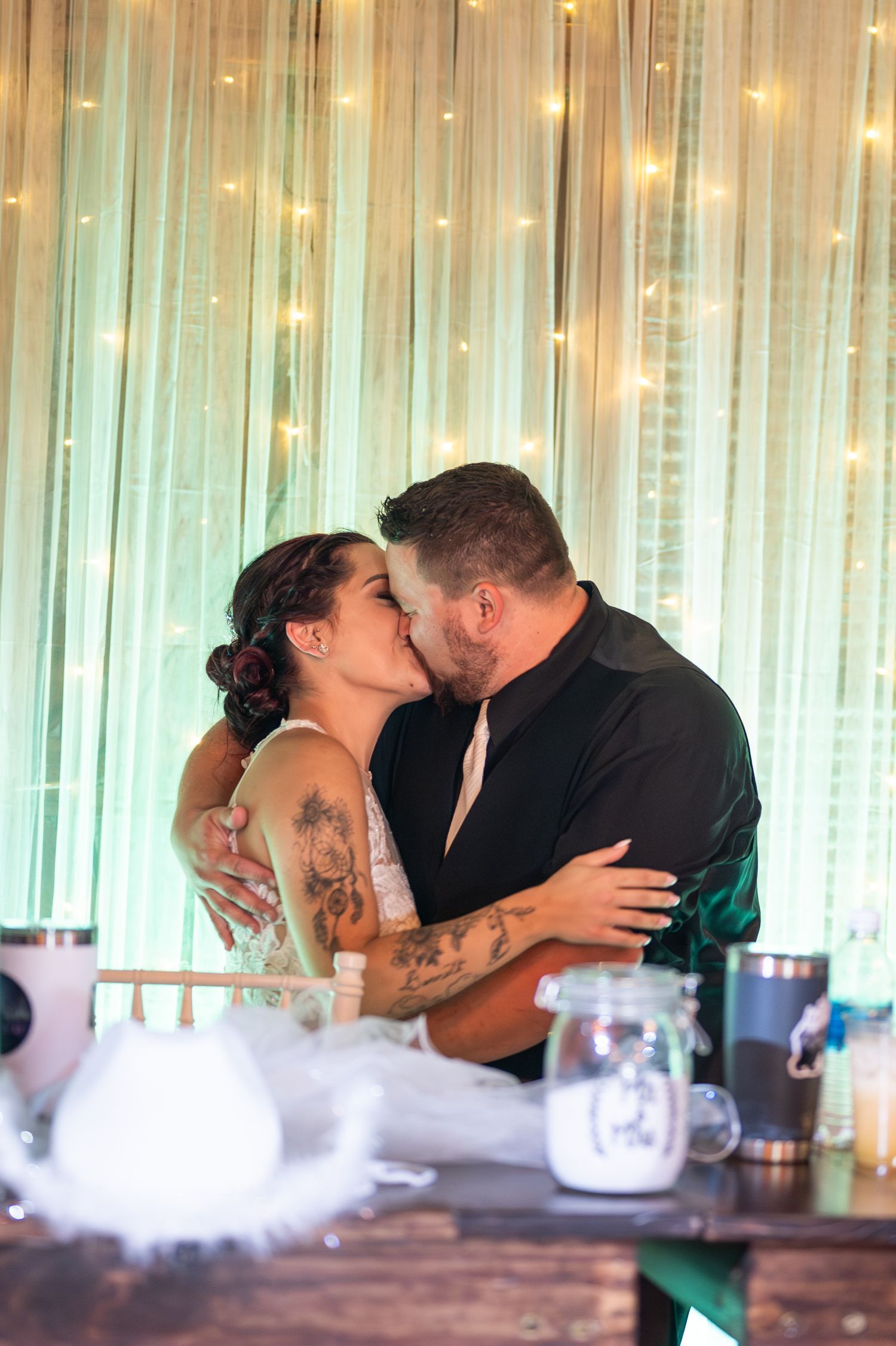 A romantic moment captured during a wedding reception with fairy lights in the background.