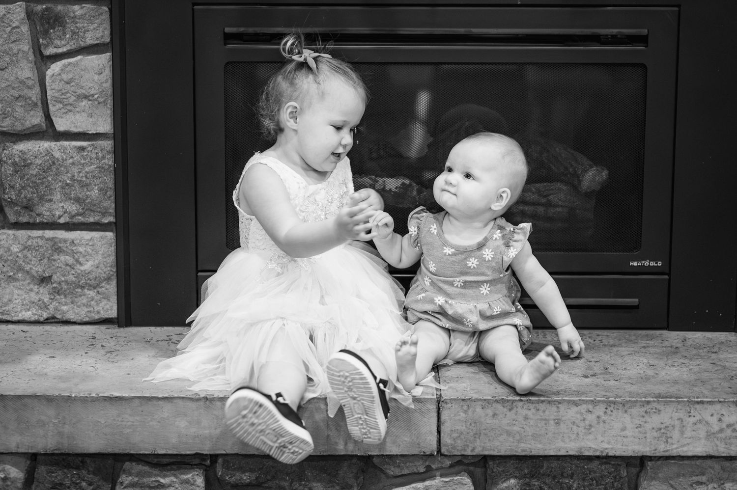 Two small children in formal wear sitting together by fireplace.