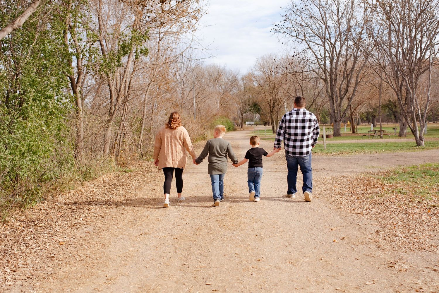 A family walking together on a dirt path surrounded by bare trees on a fall day.