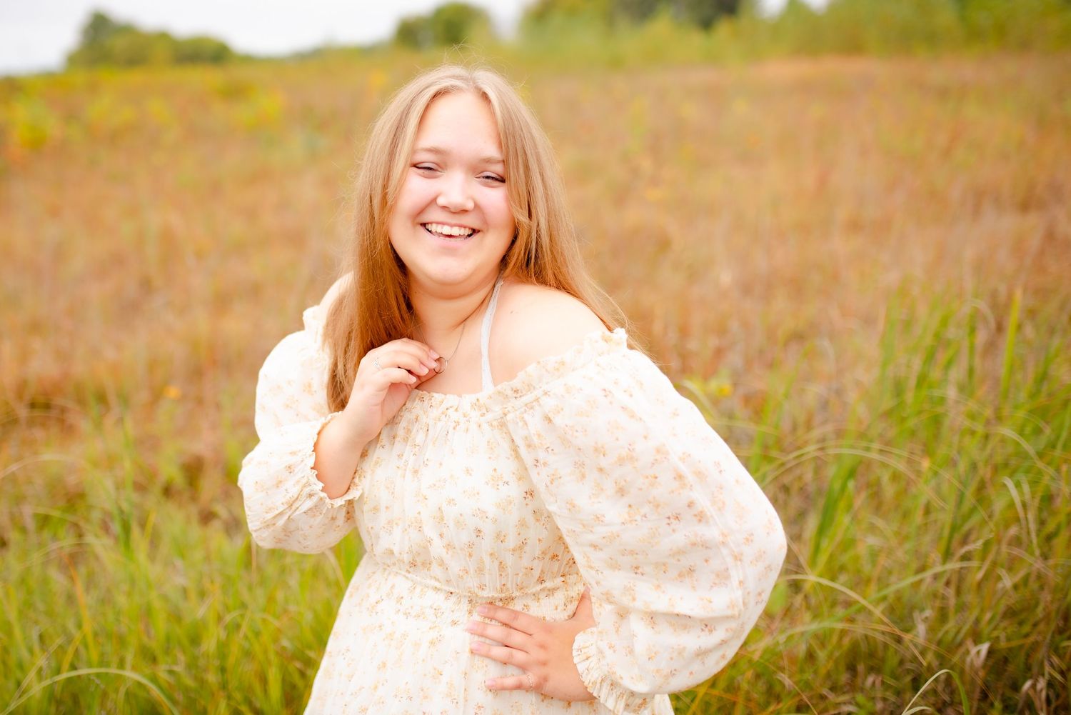 A person in a cream-colored dress poses joyfully in a golden autumn field.