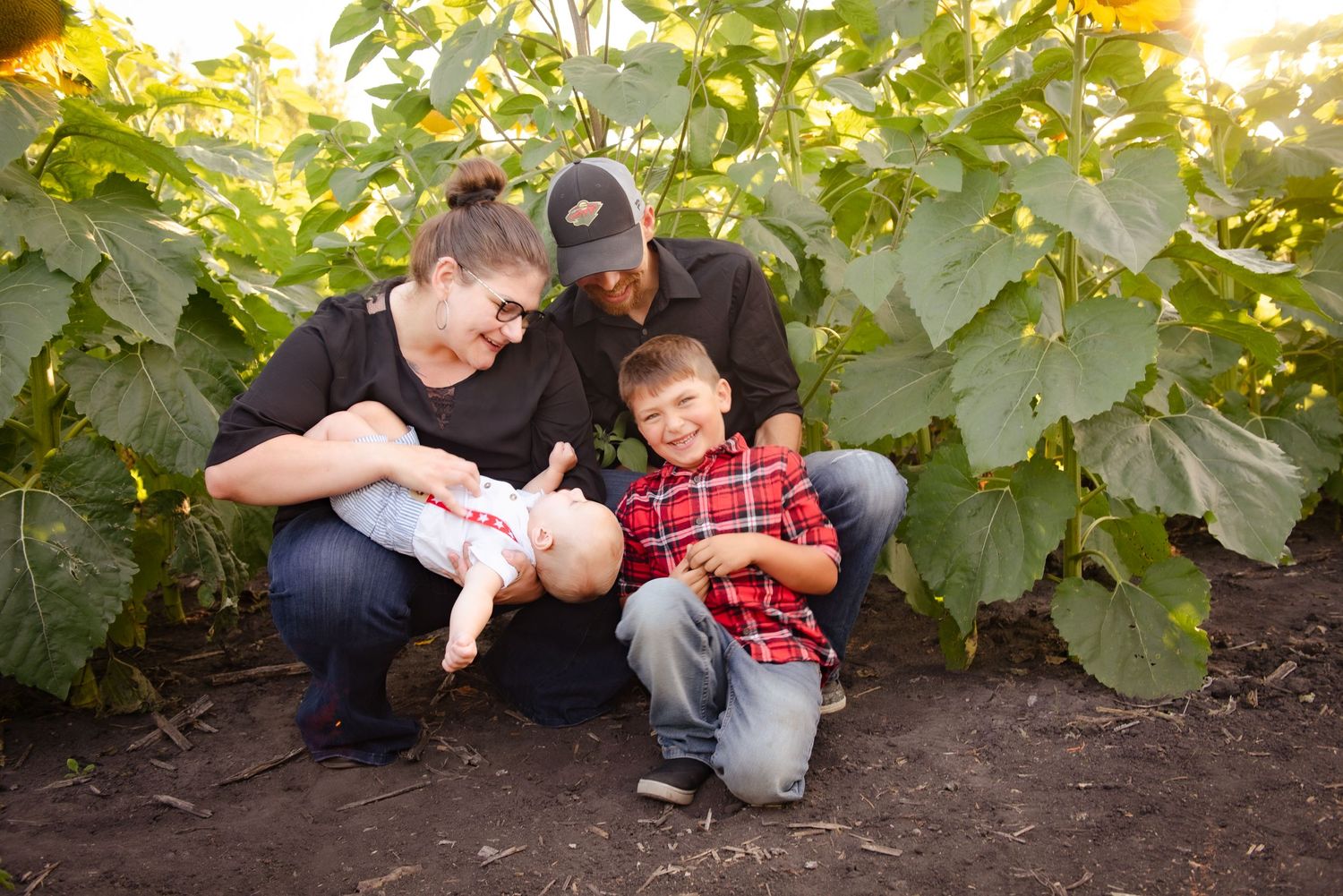 Family bonding moment captured in a sunlit garden with leafy green backdrop.