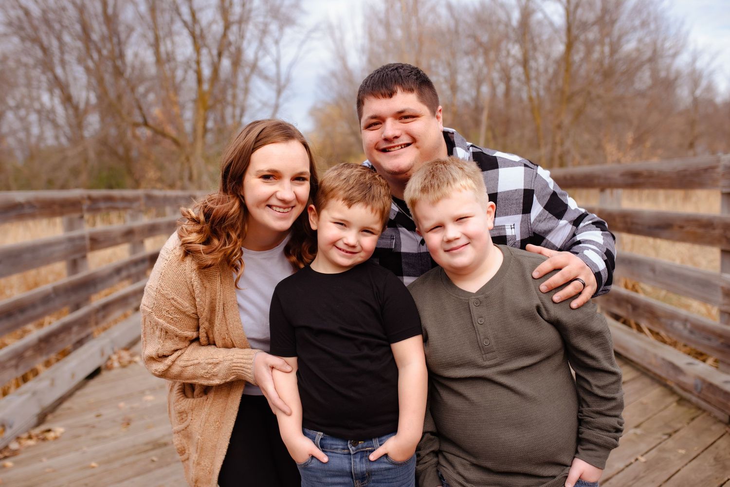 Family of four poses together on wooden bridge during autumn photo session.