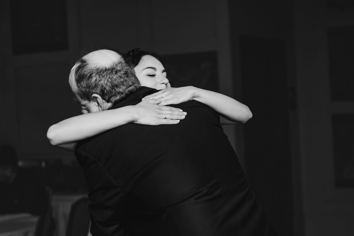 A black and white photo captures an emotional embrace during a wedding celebration.