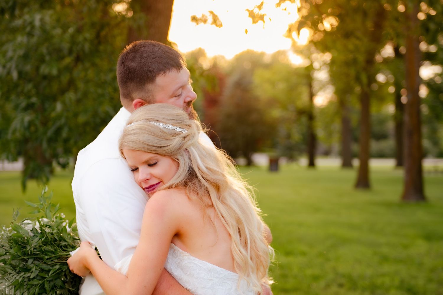 A couple shares a tender moment in a park during golden hour with sunlight streaming through trees.