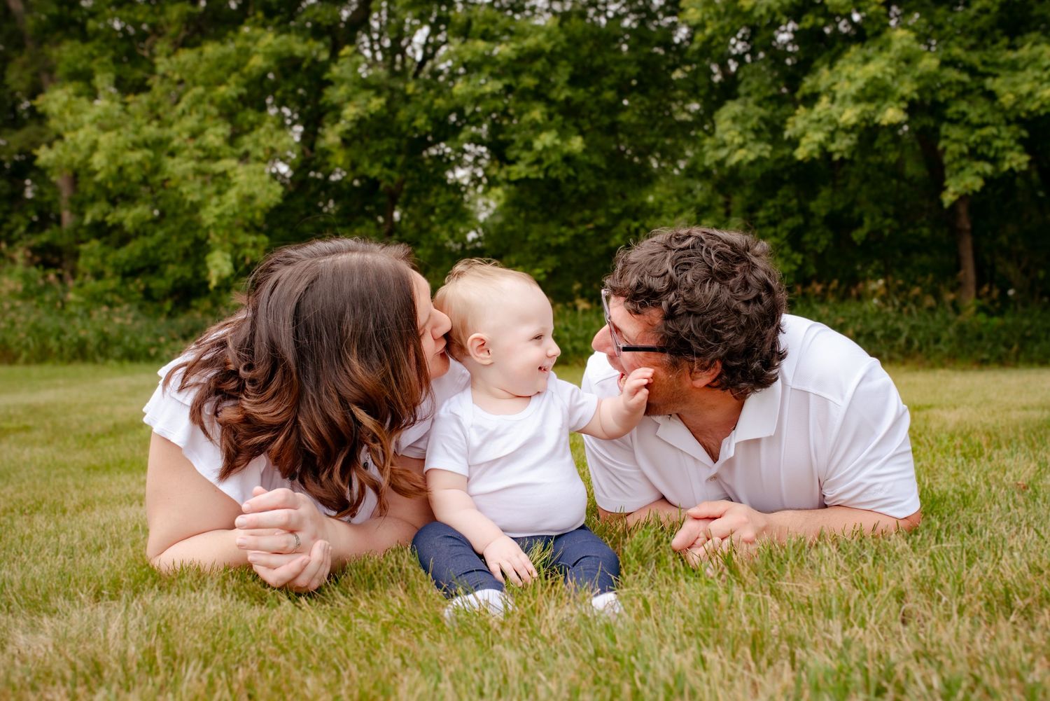 A small baby and parents lying on green grass sharing a joyful moment together.