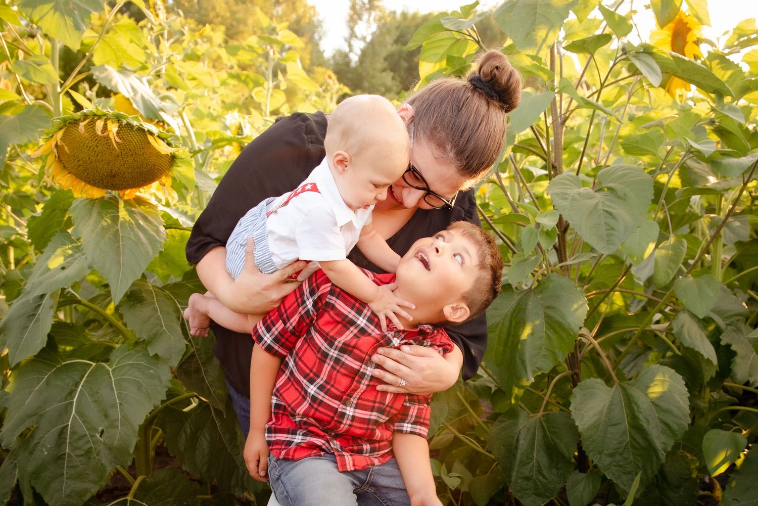 Playful family moment captured in a sunlit garden with sunflowers.