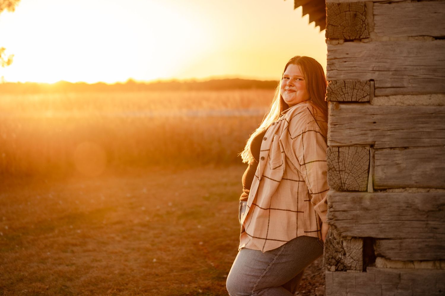 A candid sunset portrait leaning against a rustic wooden structure with golden lighting.