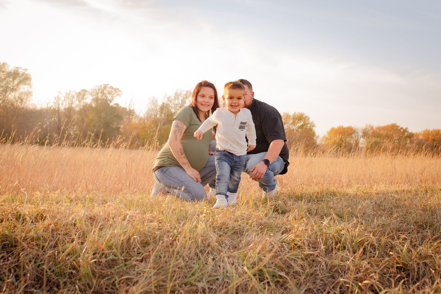 Family kneeling together in autumn field during golden hour sunset photography session.