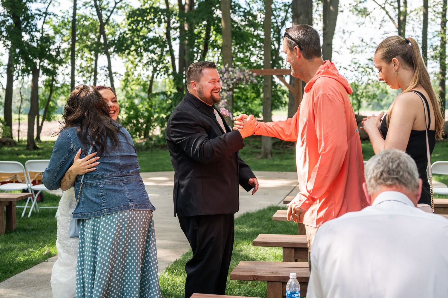 Wedding guests greet and congratulate the couple at an outdoor reception.