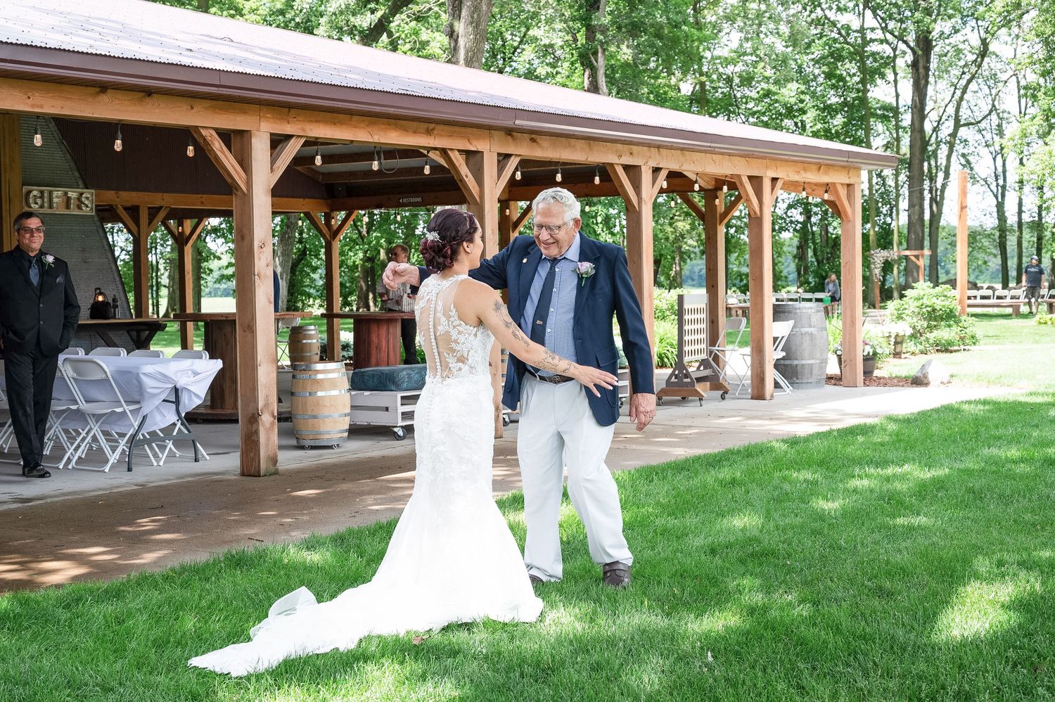 Wedding ceremony taking place under wooden pavilion on sunny day.