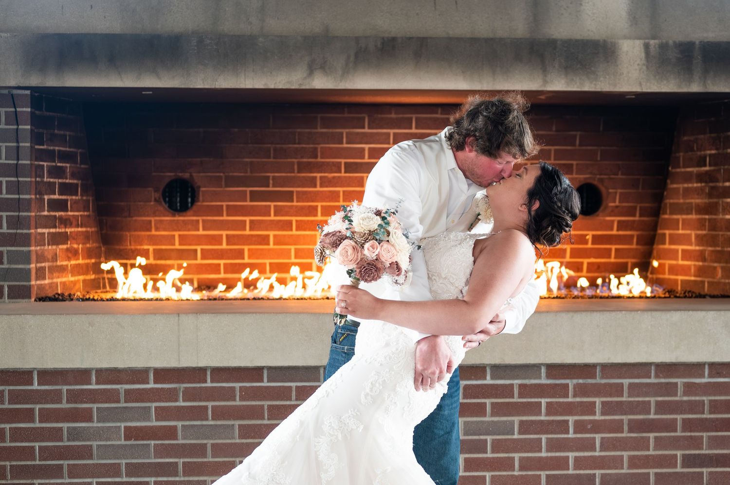 Dancing couple shares intimate moment in front of illuminated brick fireplace.