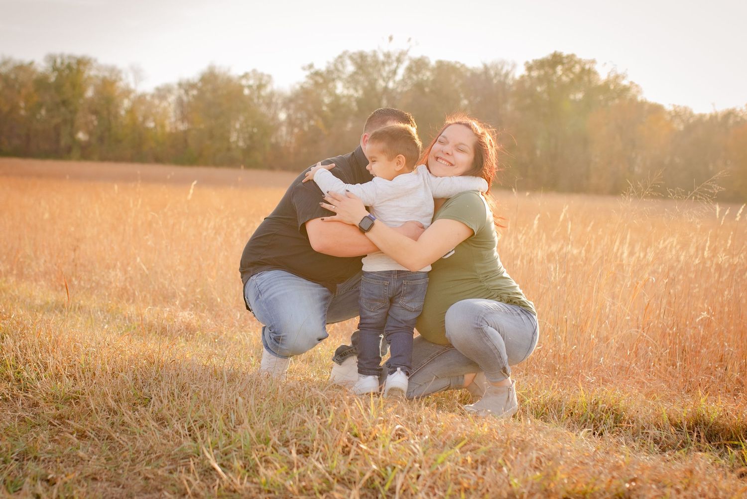 Family embracing together in a golden field during sunset.