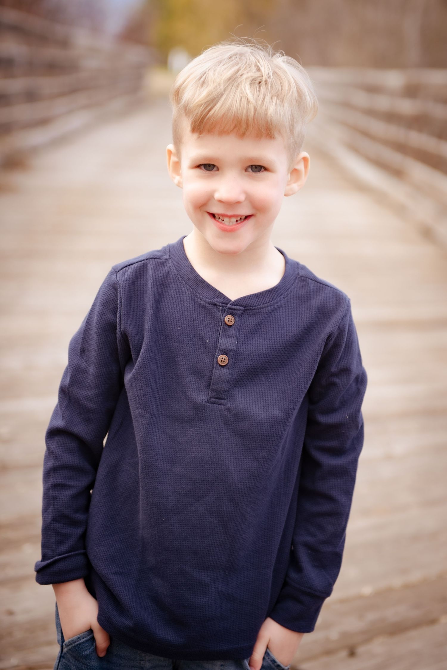 Young person in navy henley shirt standing on wooden bridge.