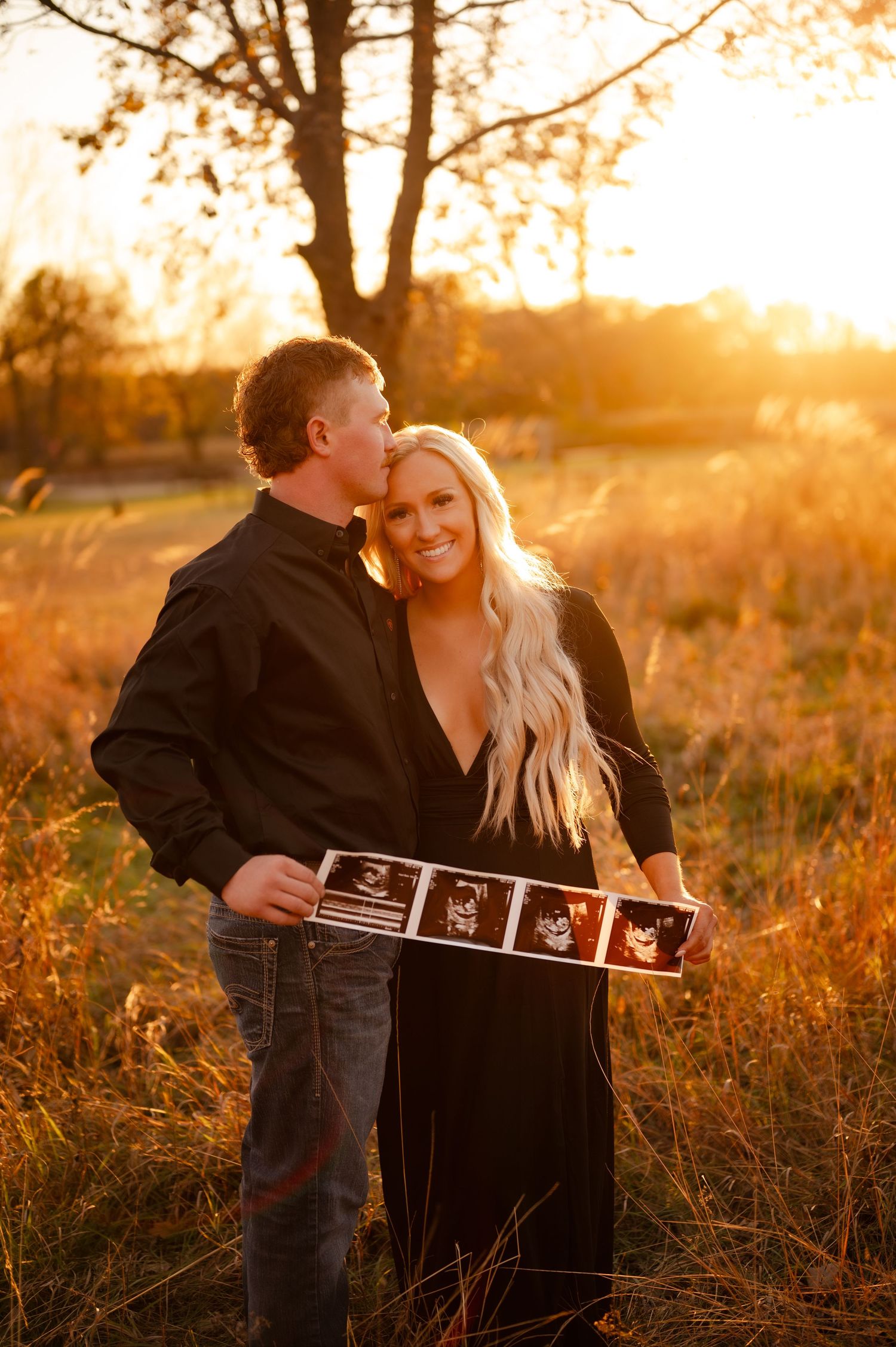 Couple holding ultrasound photos during sunset maternity photoshoot in autumn field.