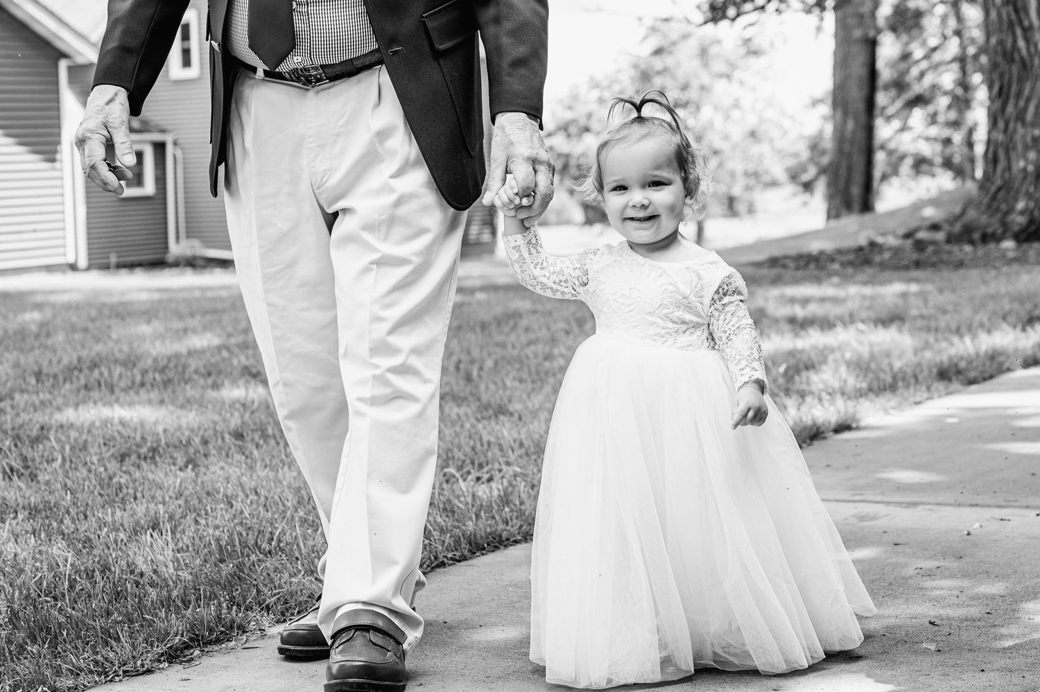 Small child in white dress walking alongside adult on pathway.