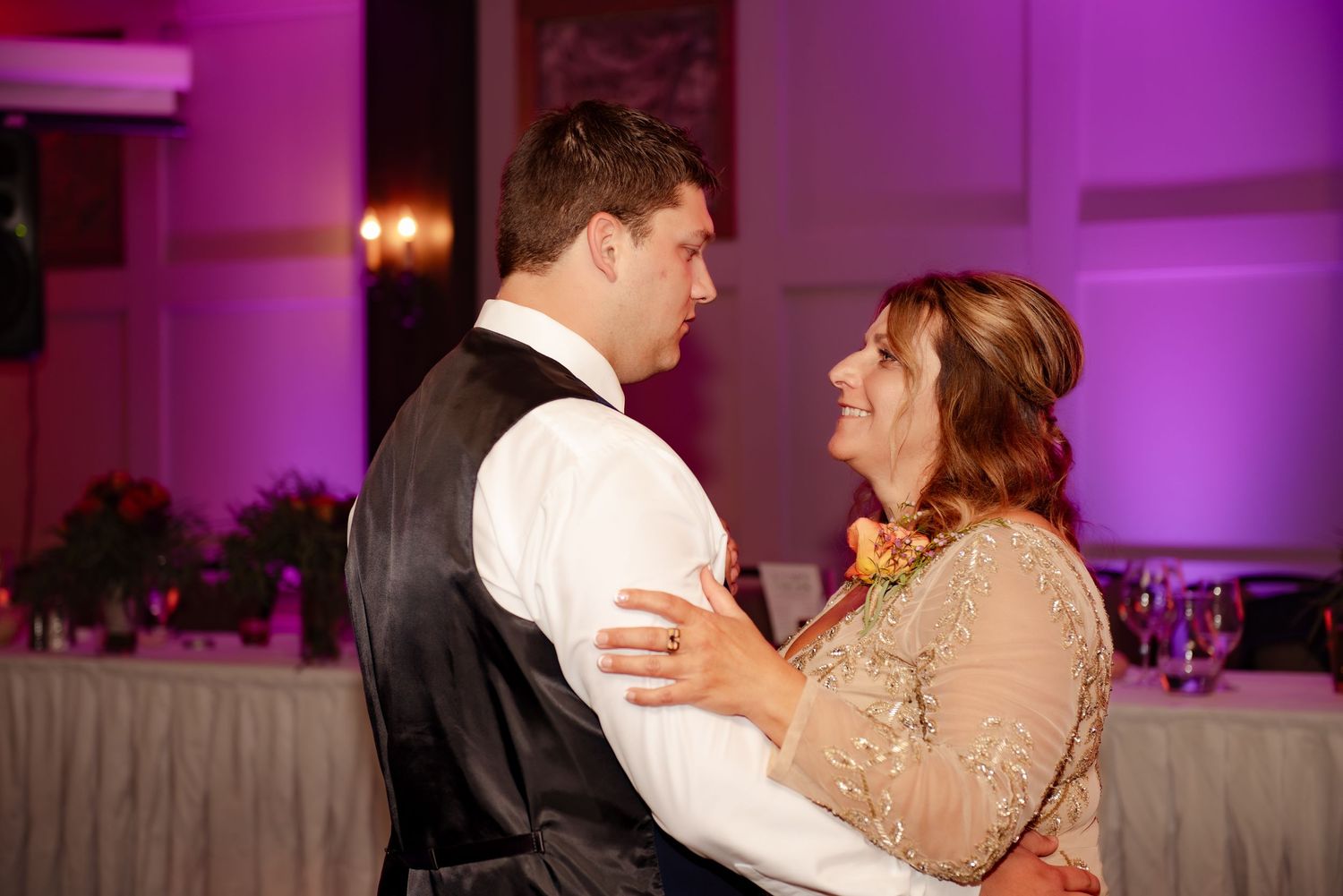 A couple shares an intimate dance moment at their wedding reception under purple lighting.
