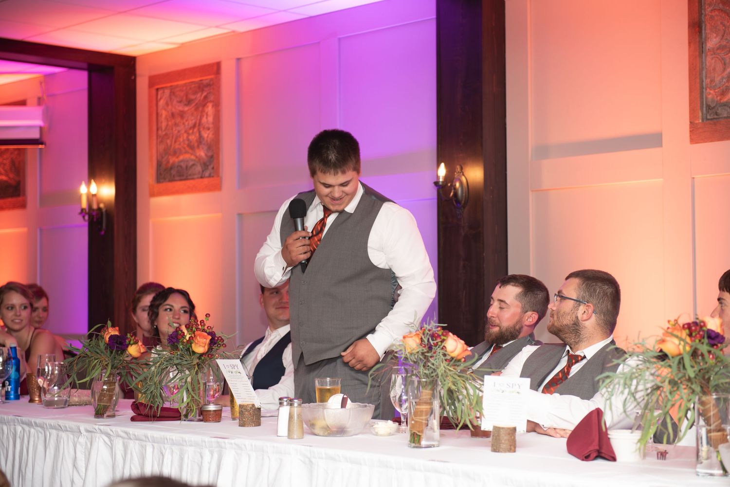 Wedding reception head table with floral centerpieces and purple uplighting during speeches.
