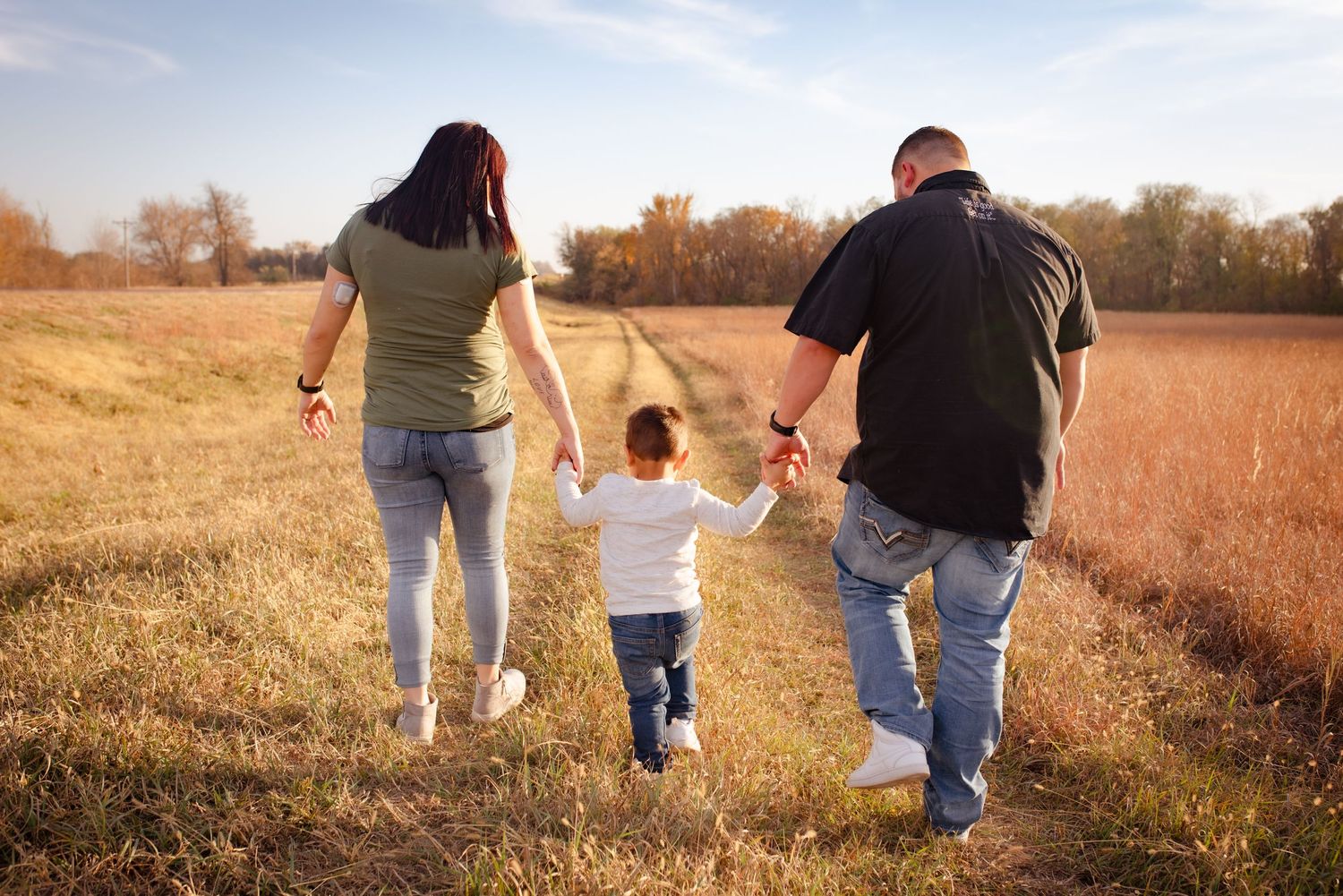 Family walking hand in hand through a sunlit autumn field together.