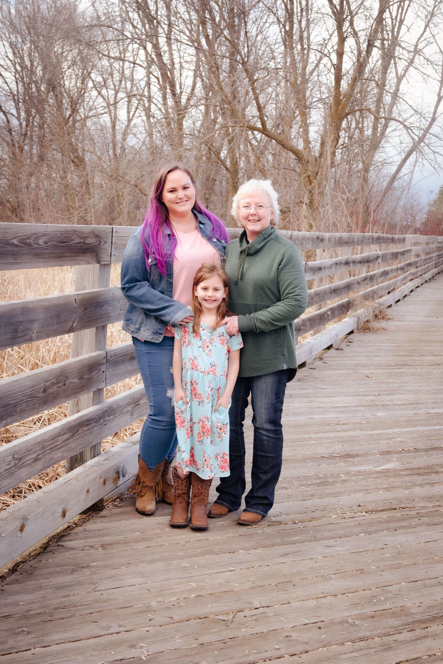 Three generations of family members pose together on wooden bridge.