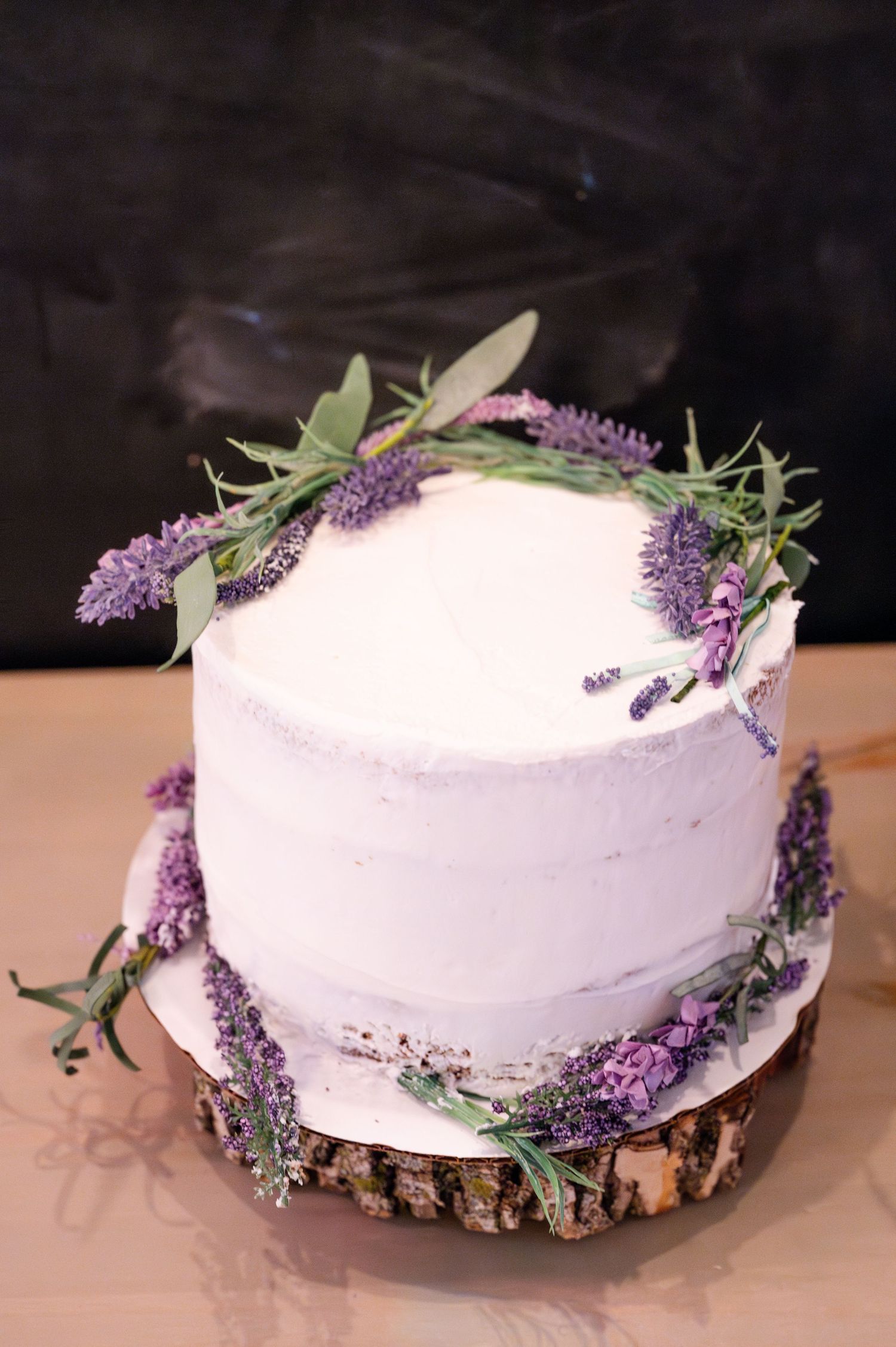 Elegant white wedding cake decorated with fresh lavender sprigs on wooden slice base.