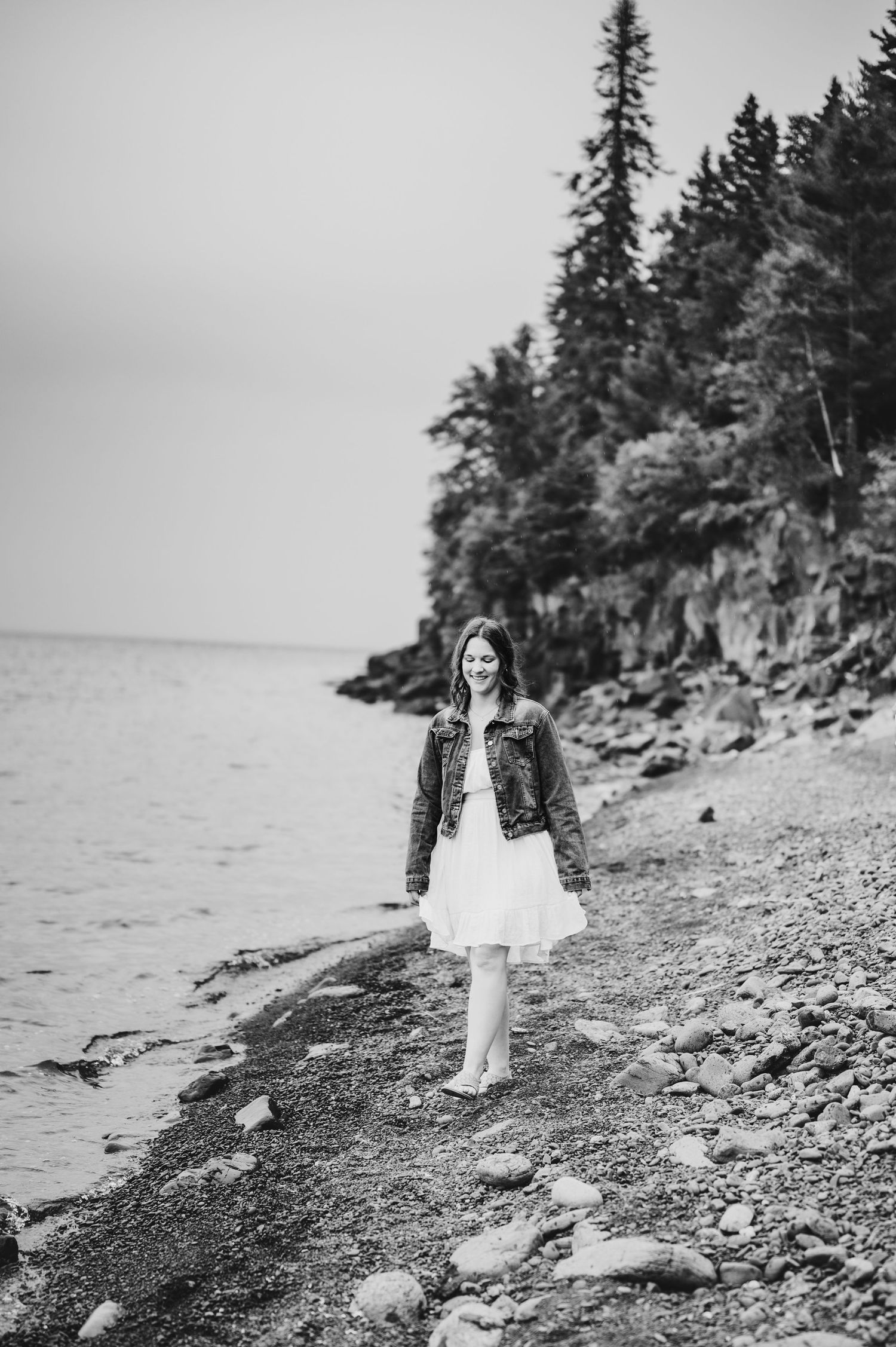 Black and white portrait of person in denim jacket and dress on rocky coastline.