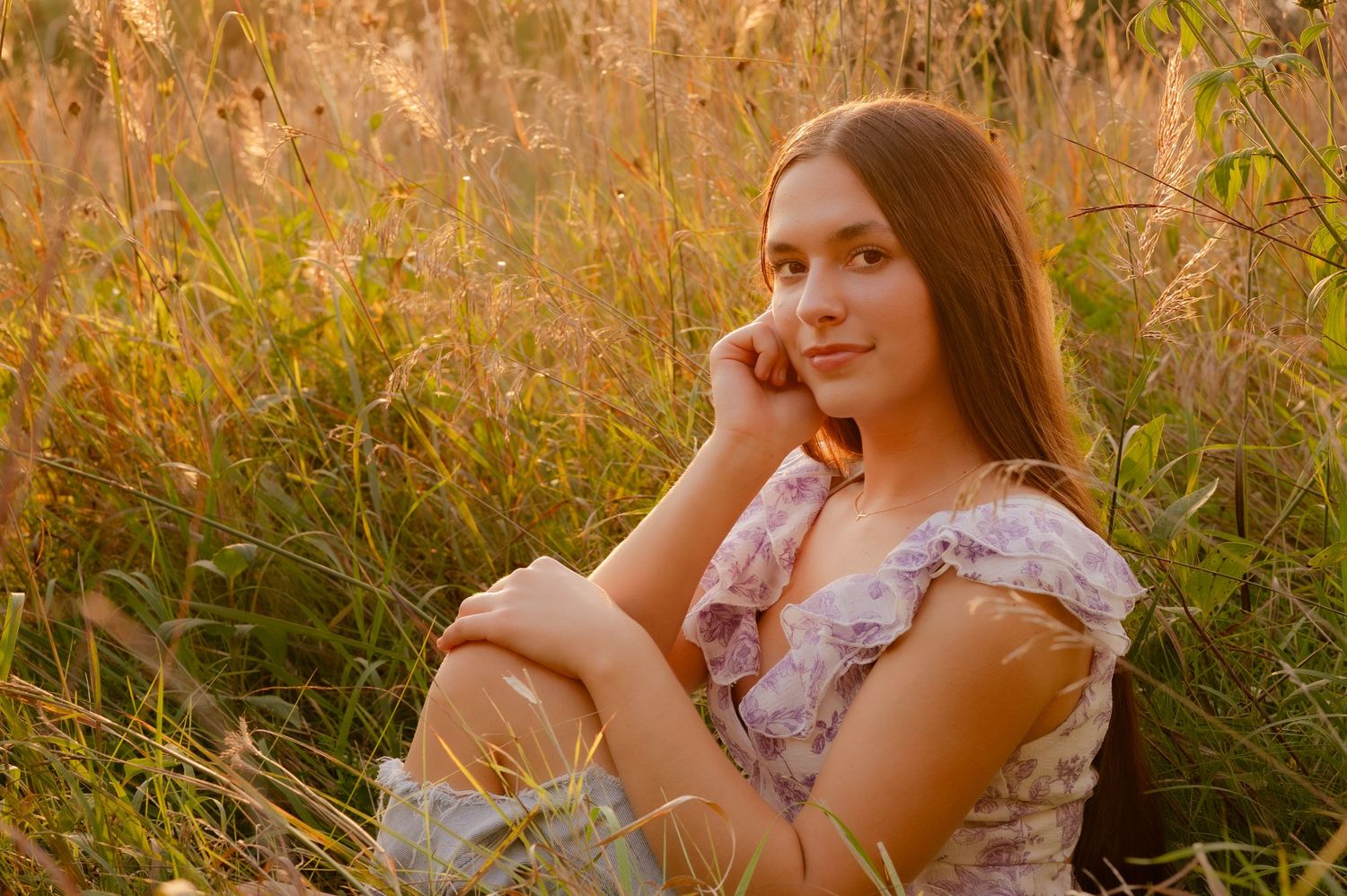 Woman in floral dress poses in golden field during sunset creating dreamy summer portraits.