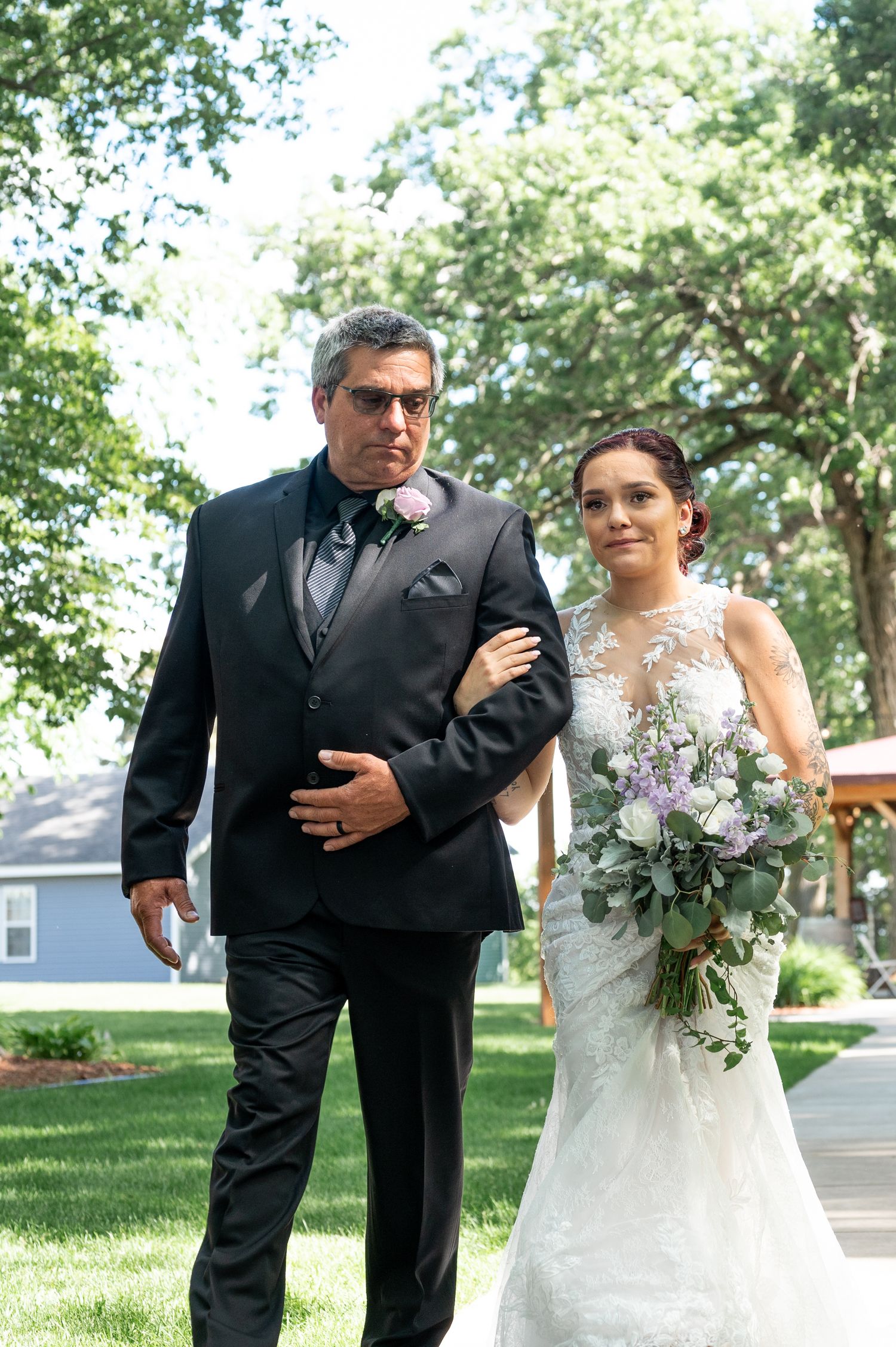 Wedding procession walking down outdoor pathway with beautiful bouquet and formal attire.