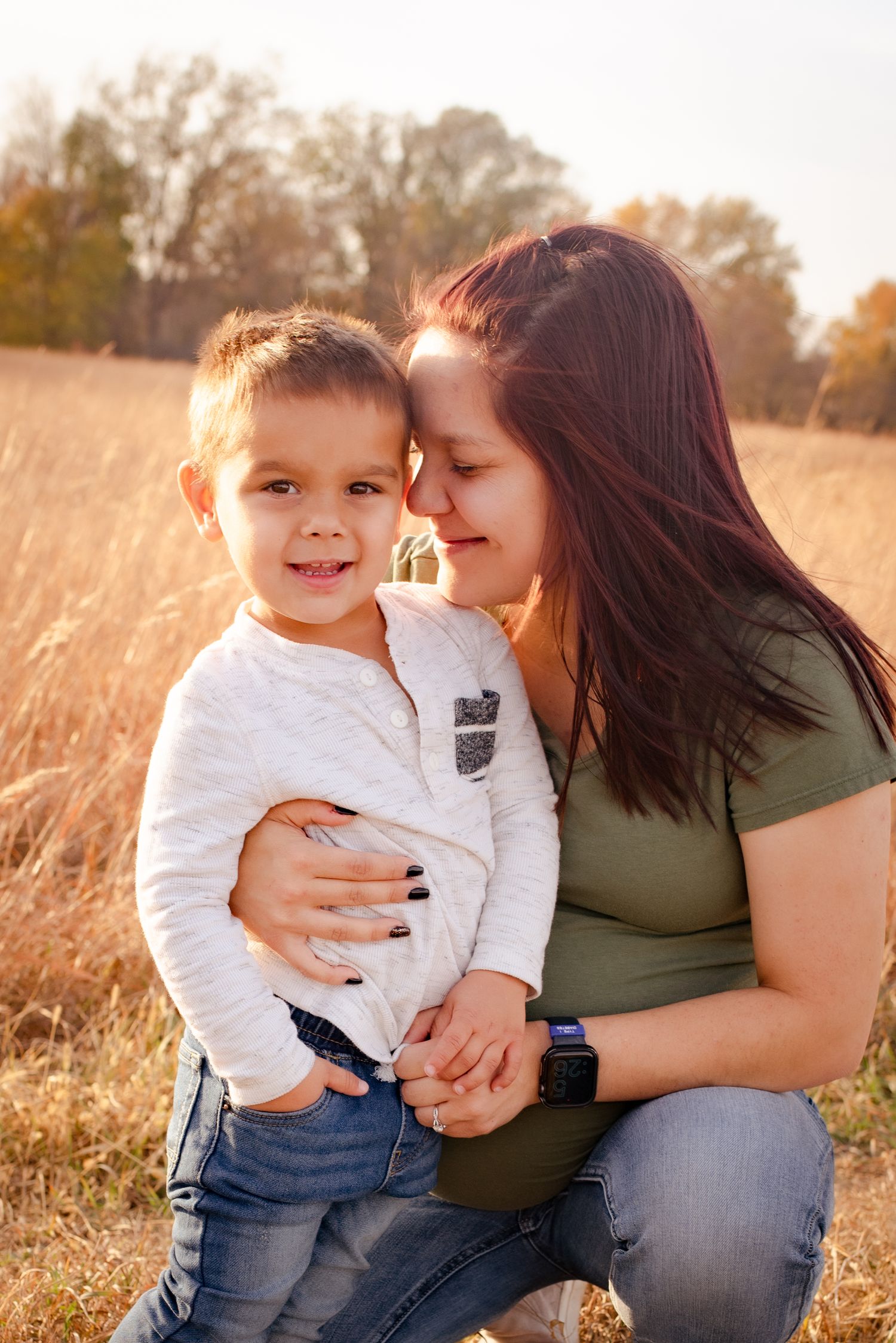 Intimate family portrait captured in warm autumn sunlight among tall grass.