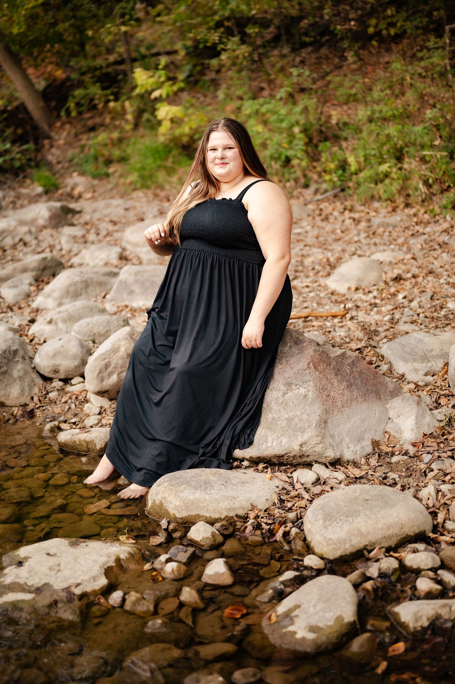 A scenic outdoor portrait by a rocky creek bed featuring a flowing black maxi dress.