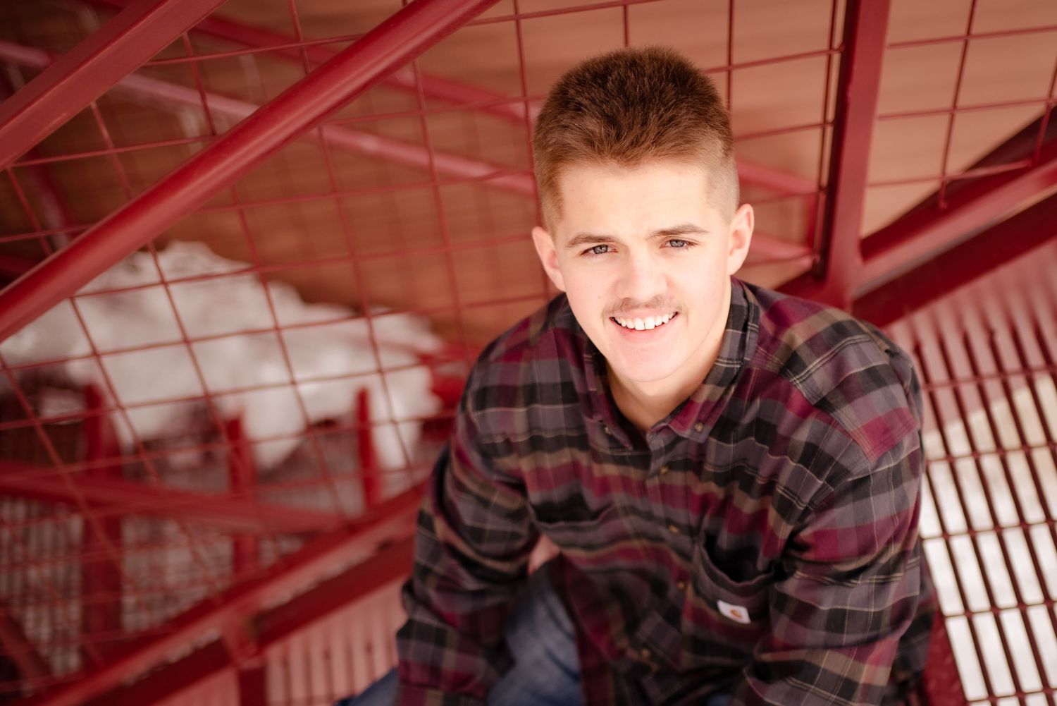 Young person in plaid shirt smiles while sitting on red metal staircase.