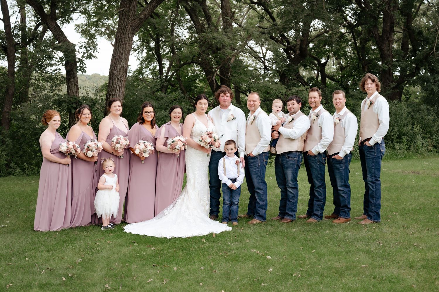 Wedding party in pink dresses and casual attire posed together outdoors.