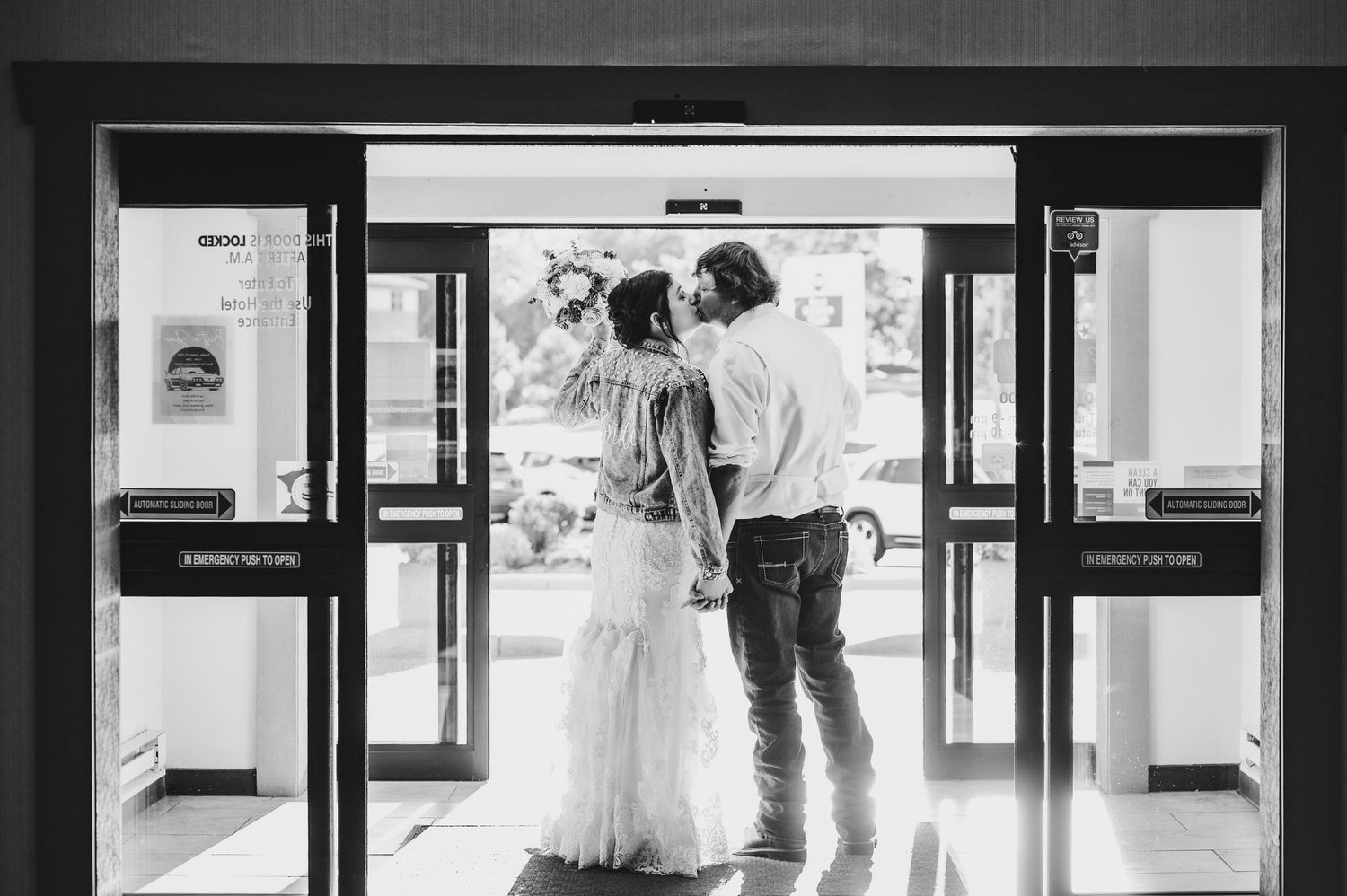 Black and white image of a couple standing in silhouette at glass entrance doors.