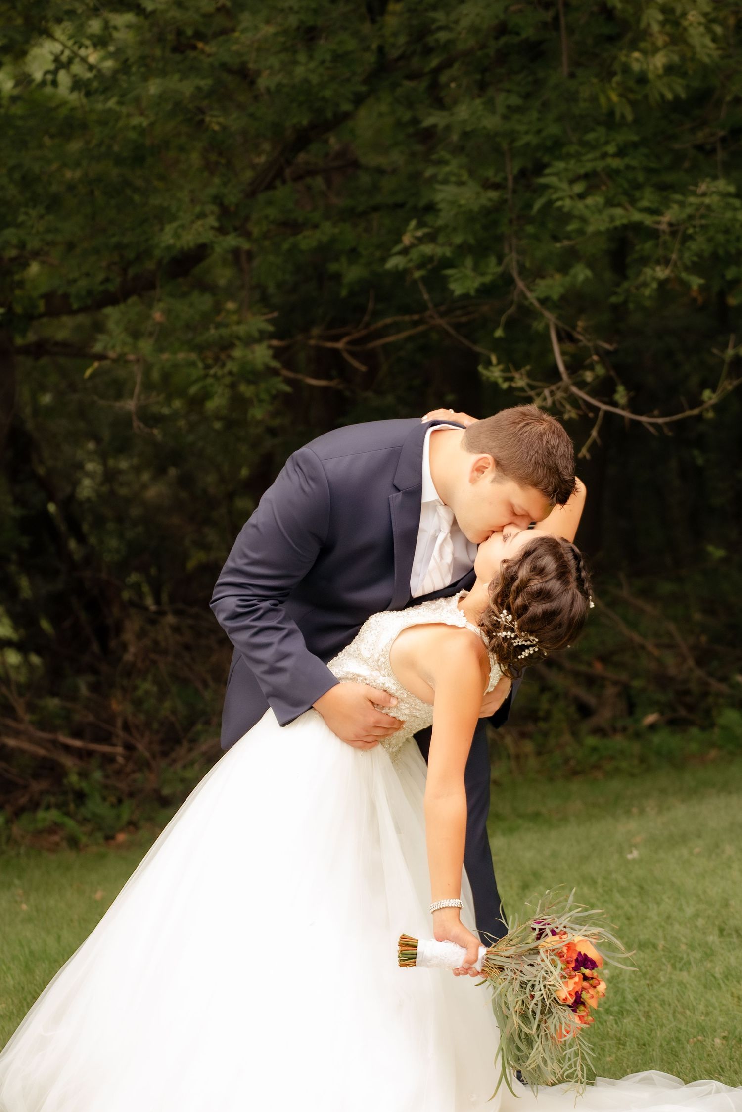 Dramatic dip kiss between bride and groom in a garden setting with autumn bouquet.