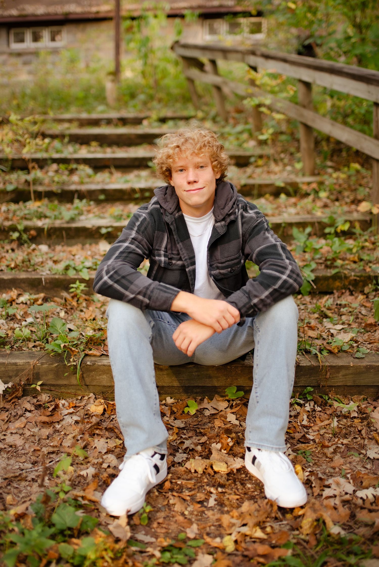 A casual portrait of someone sitting on wooden steps surrounded by fallen autumn leaves.