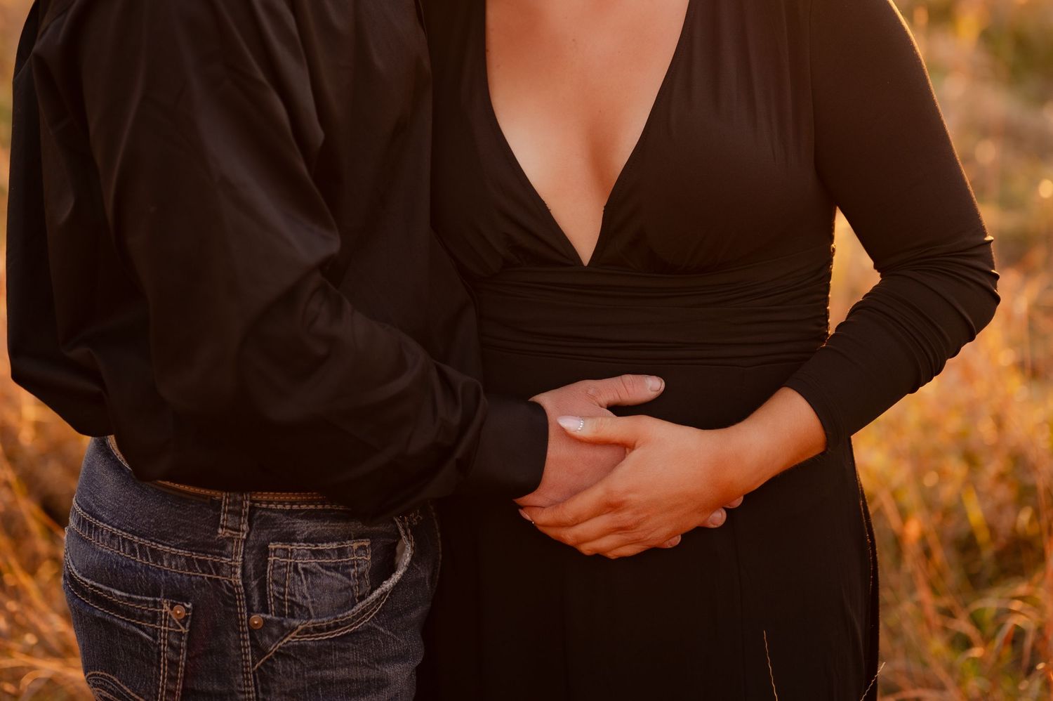 A couple in casual attire embracing during golden hour with jeans and a black top against an autumn background.