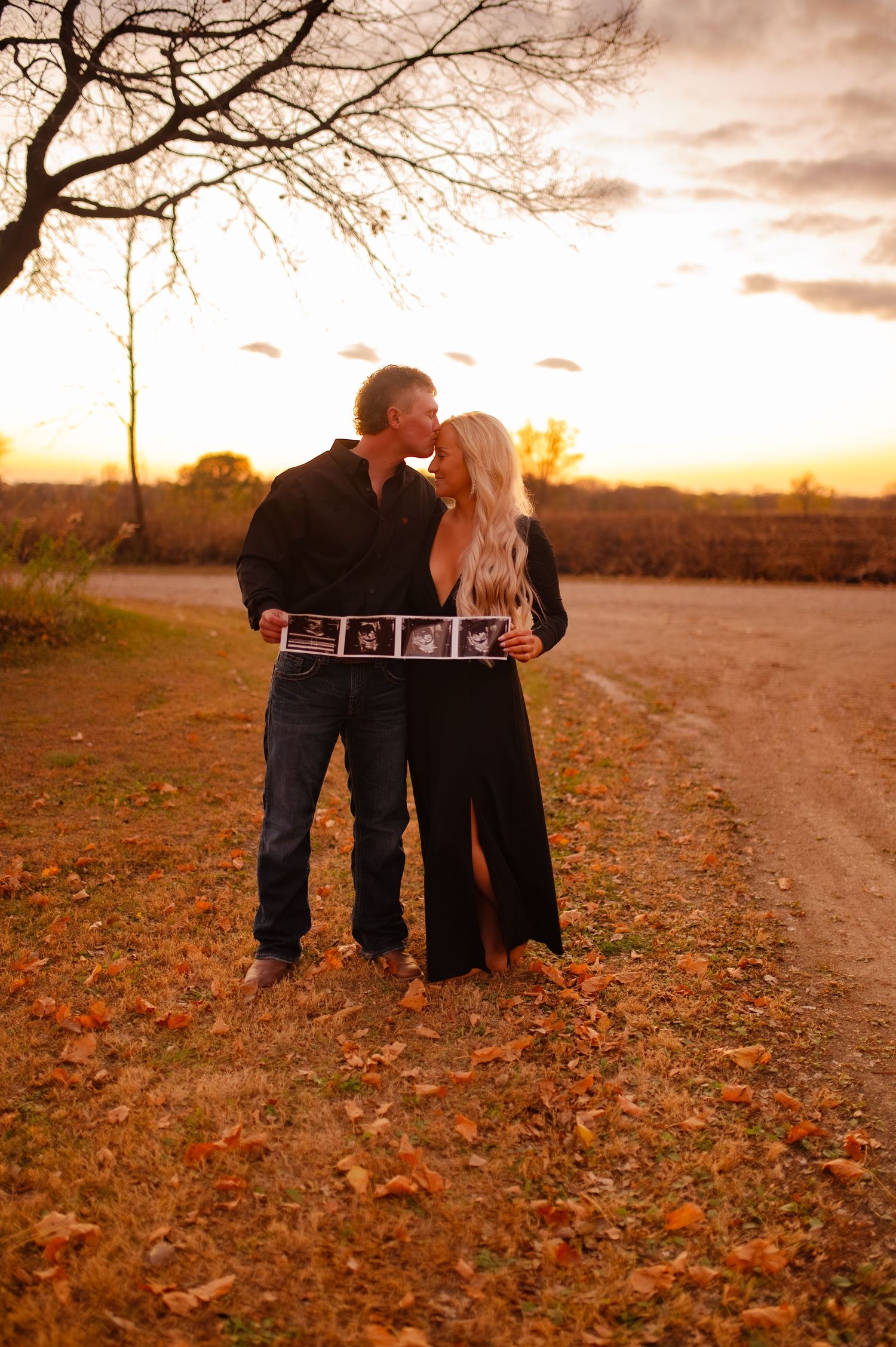 Two people share tender moment on autumn path with ultrasound photos.