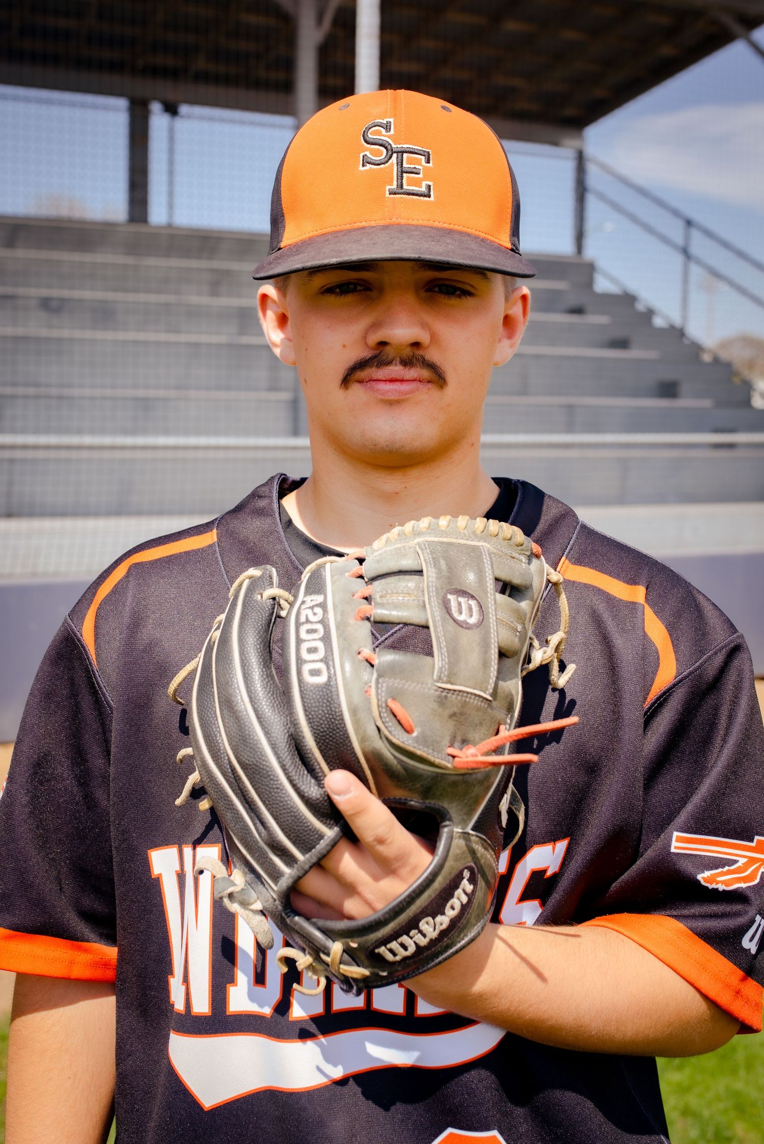 Baseball player in navy and orange uniform poses with Wilson glove on field.