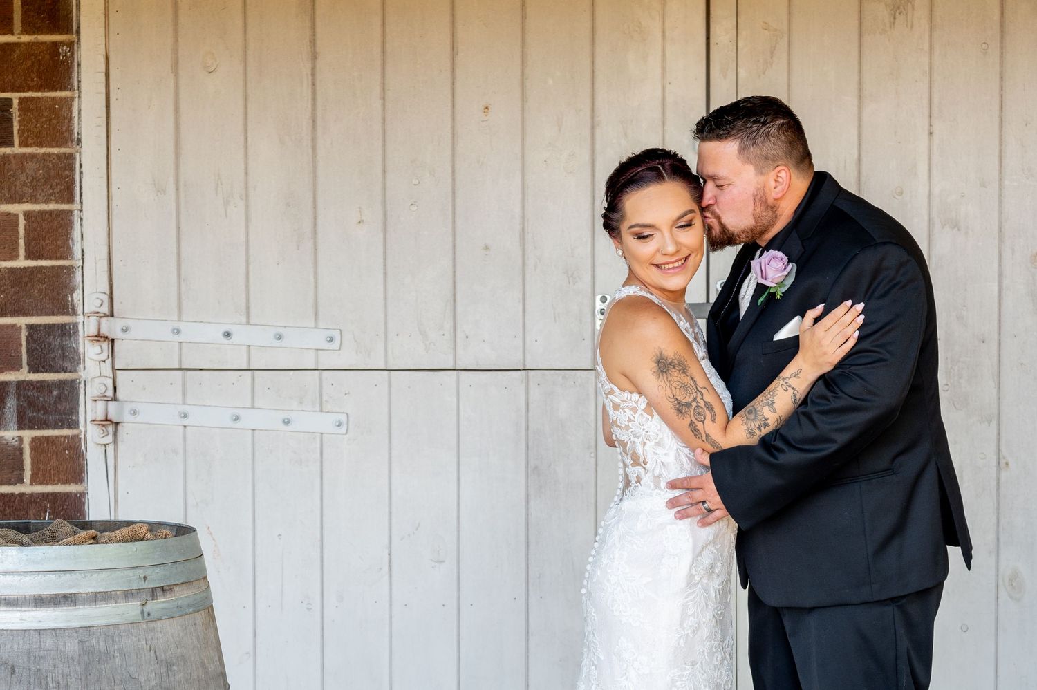 Intimate moment between newlyweds laughing together against white wooden barn doors.