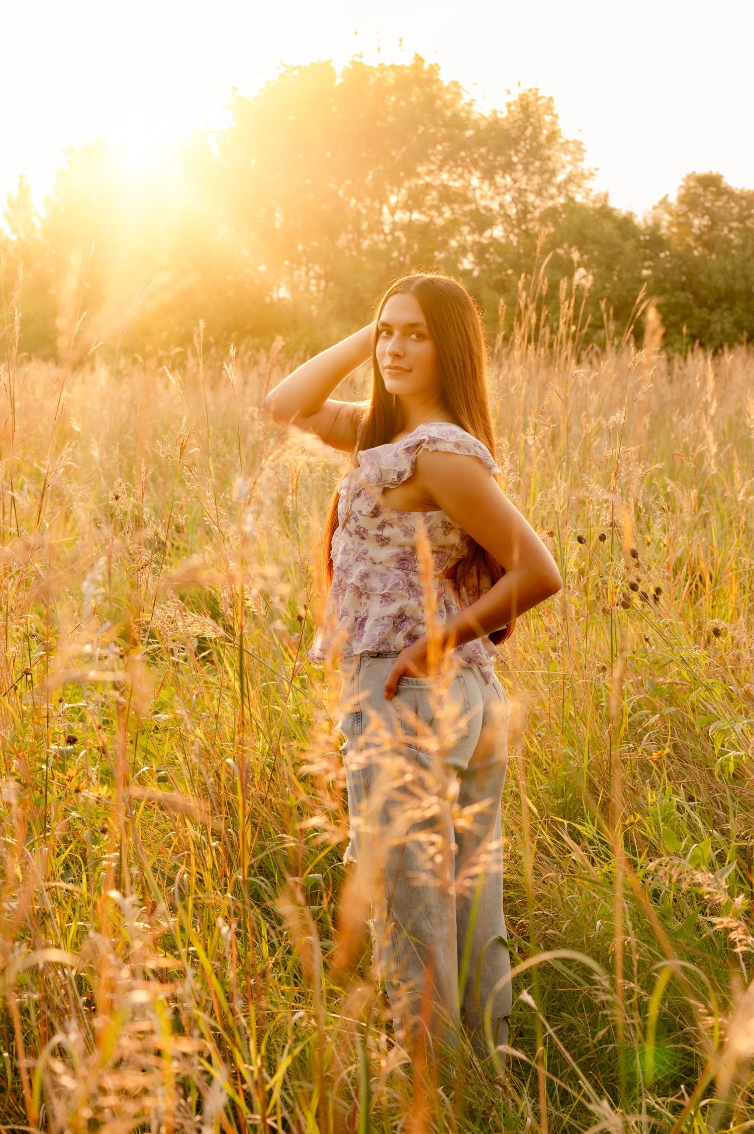 Person in a floral dress poses gracefully in a golden sunlit meadow during sunset.