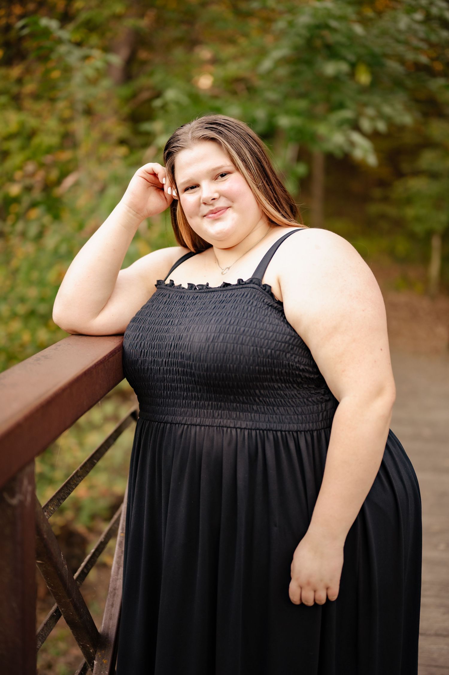 A portrait on a wooden bridge featuring a black maxi dress against a natural wooded background.