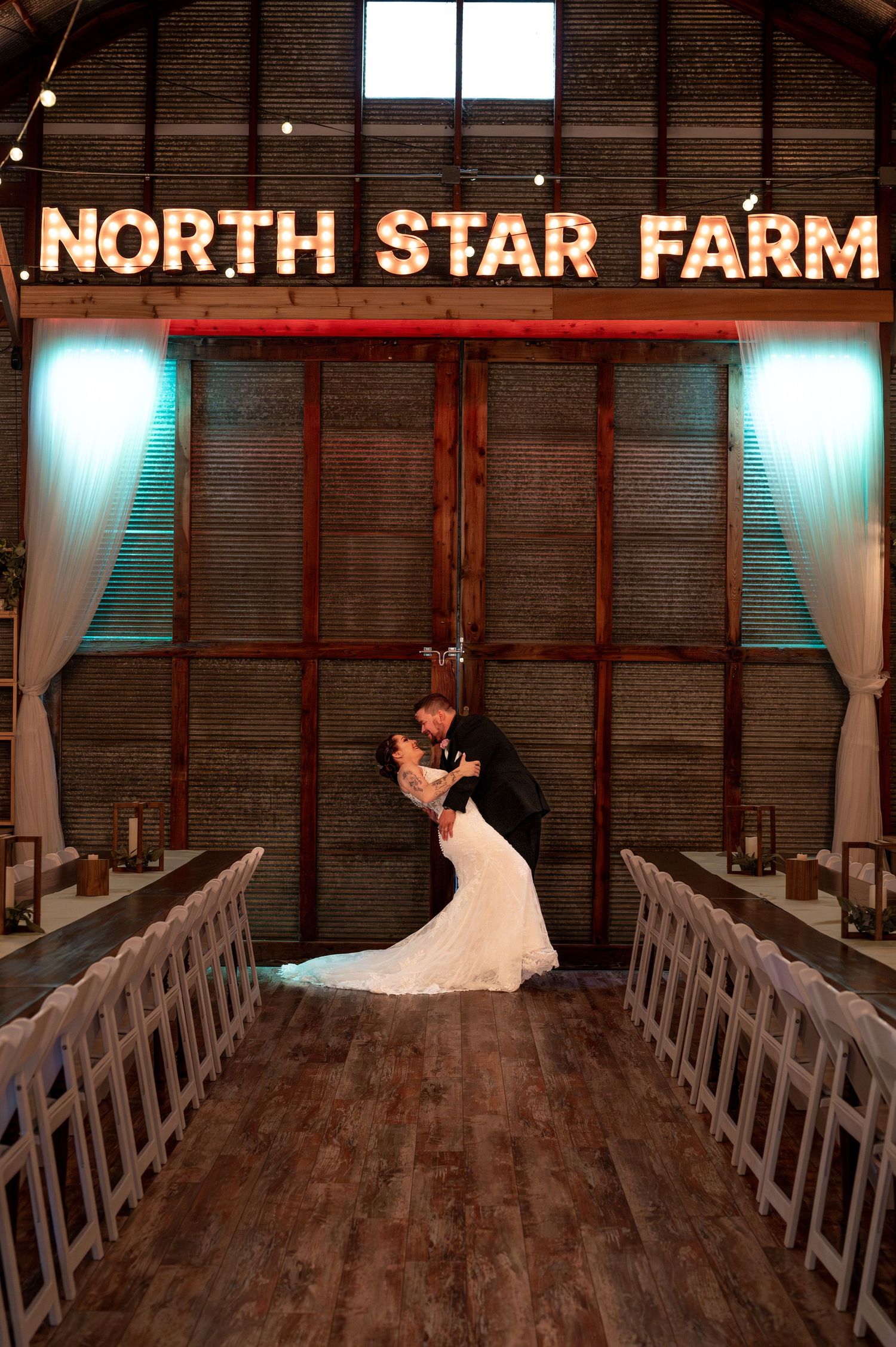 Romantic wedding photo inside rustic barn venue with North Star Farm illuminated sign.