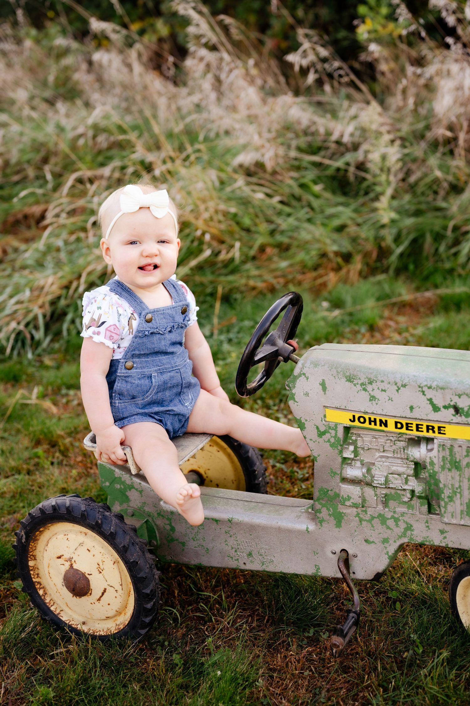 Toddler smiles while sitting in classic pedal-style John Deere toy tractor outdoors.